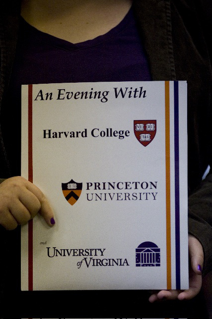 Woman holding a sign that says: An evening with Harvard College, Princeton University and the University of Virginia