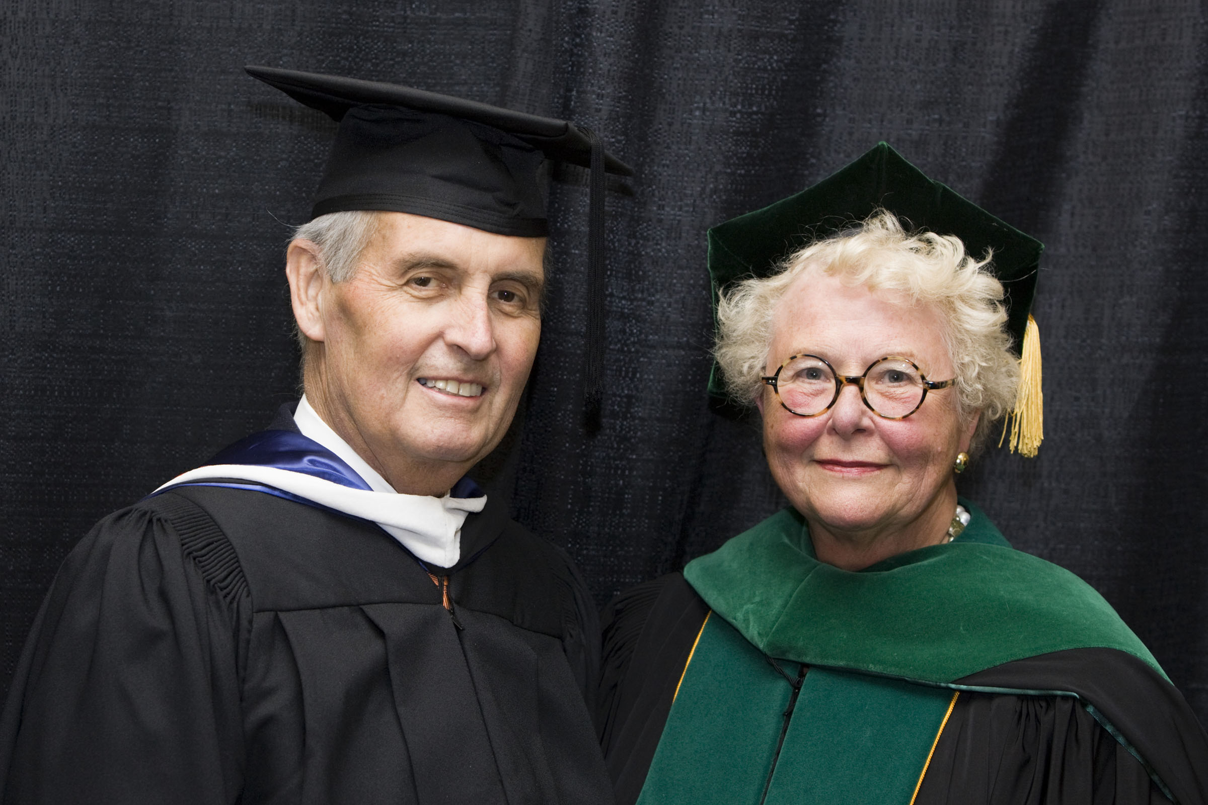 Jack Blackburn and Dr. Sharon Hostler stand next to each other dressed in caps and gowns smiling at the camera