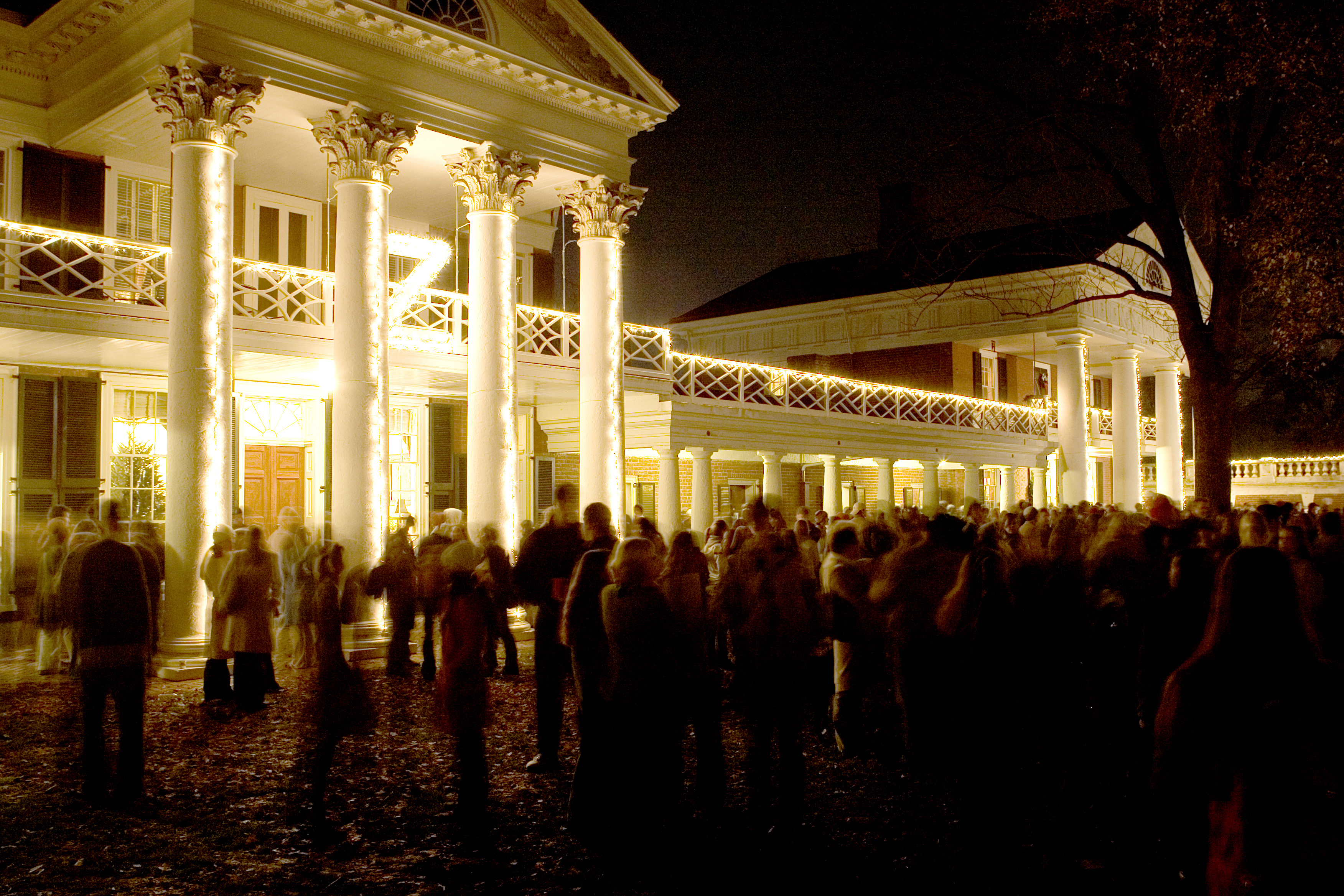 Crowd gathered on the lawn while the buildings are outlined in white lights