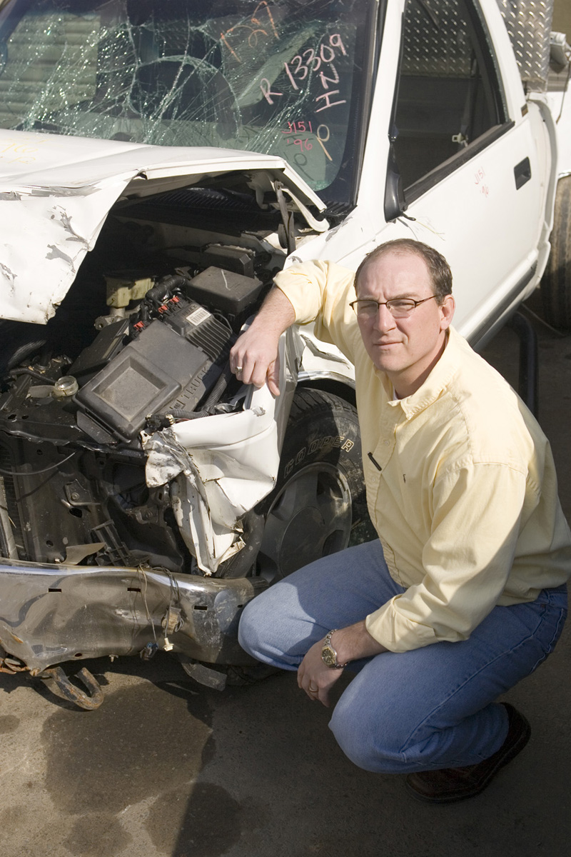 Richard Kent bends down next to a crashed car