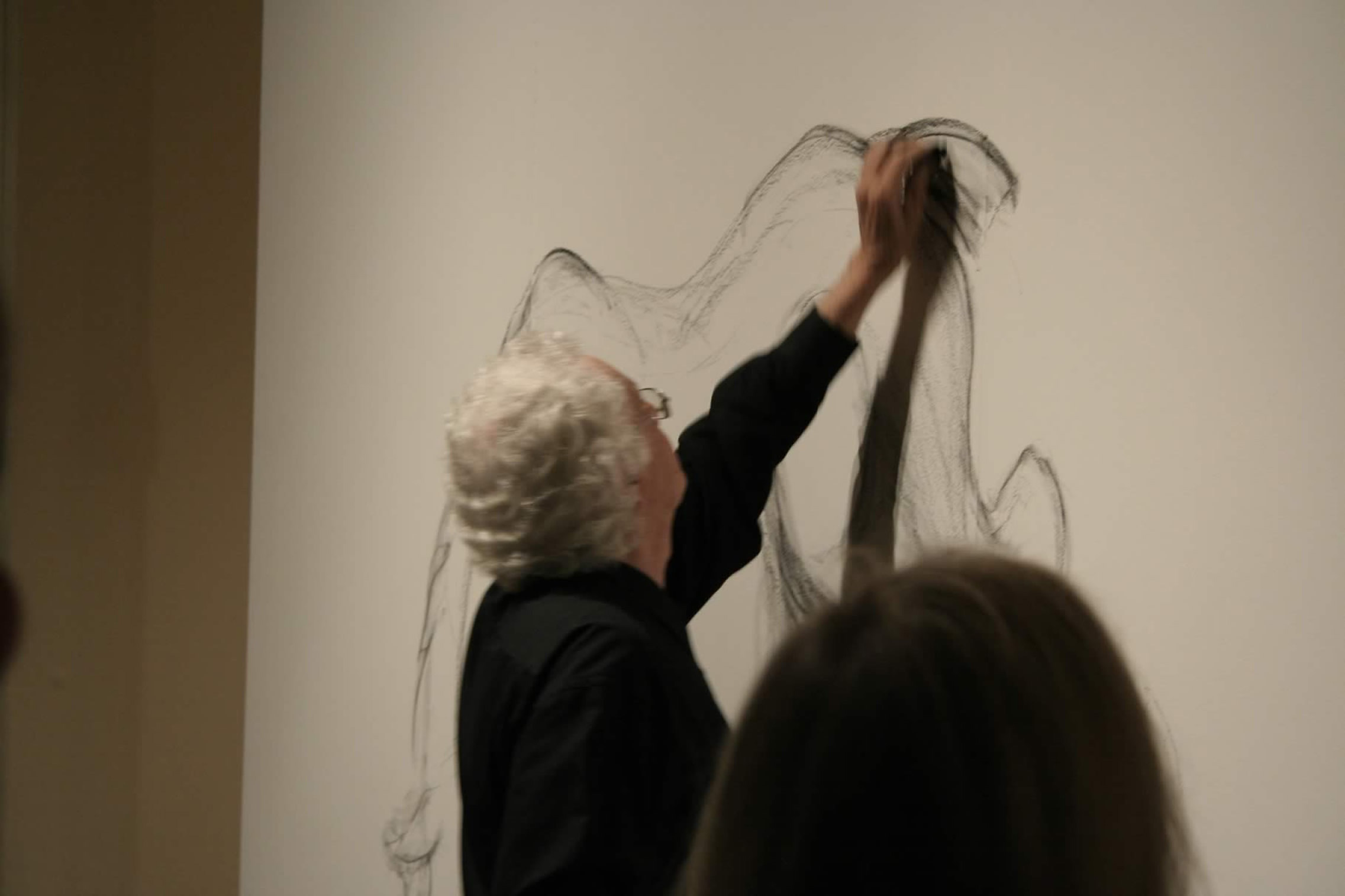 Patrick Oliphant drawing on a wall while people watch