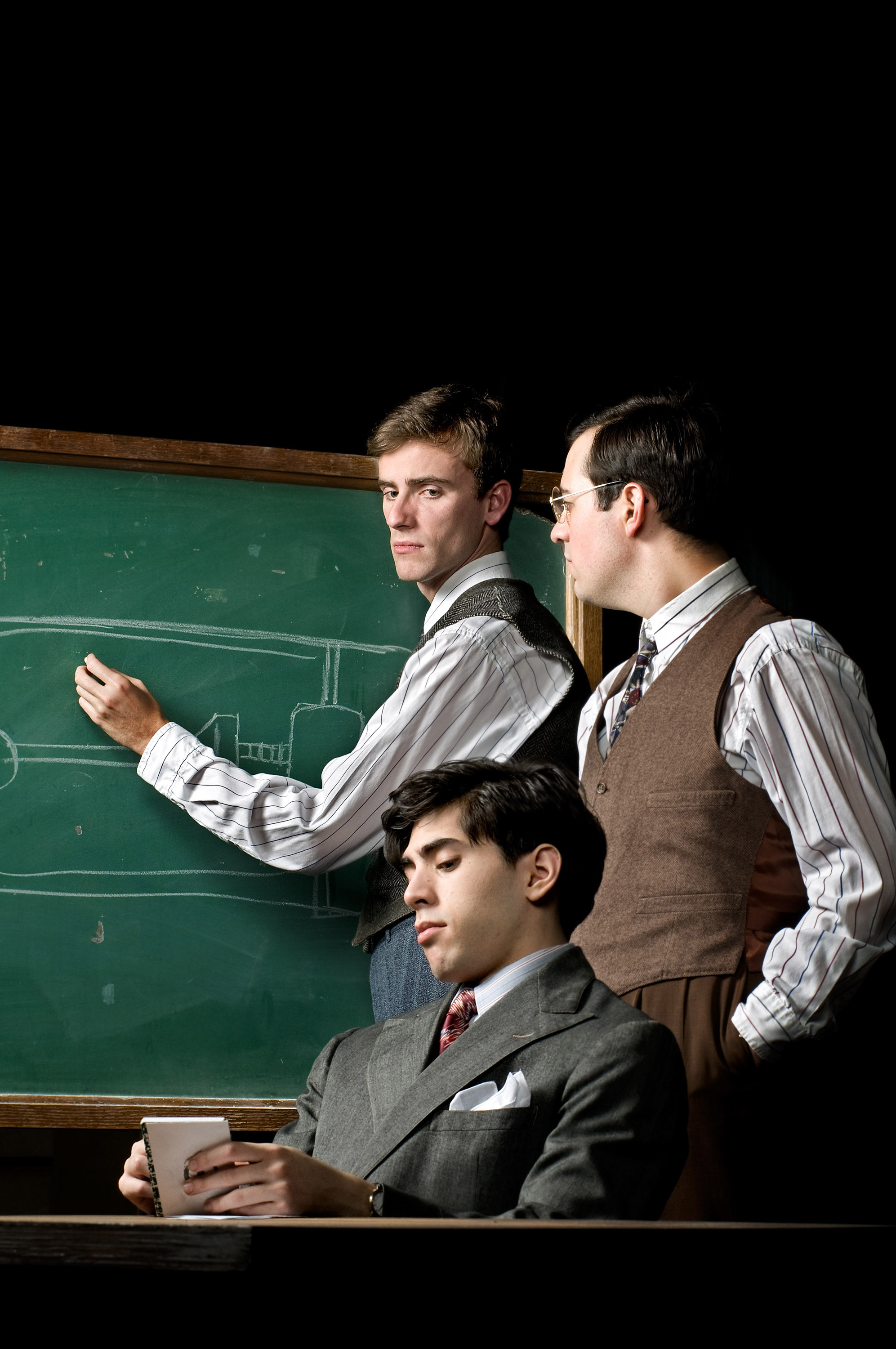 Three actors dressed in suits pose on stage with a chalkboard for a picture
