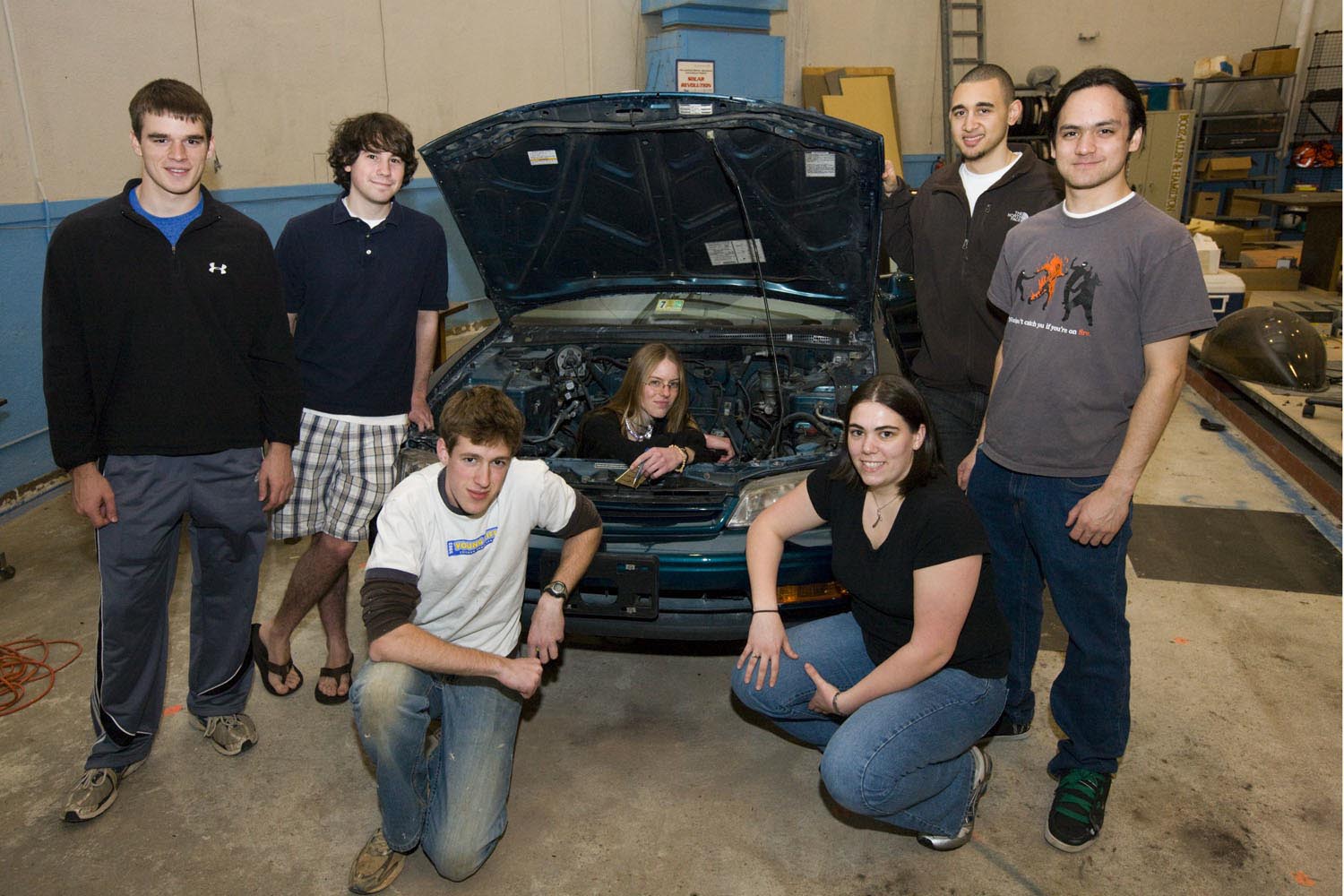 Group of students stand in front of a car in a repair shop