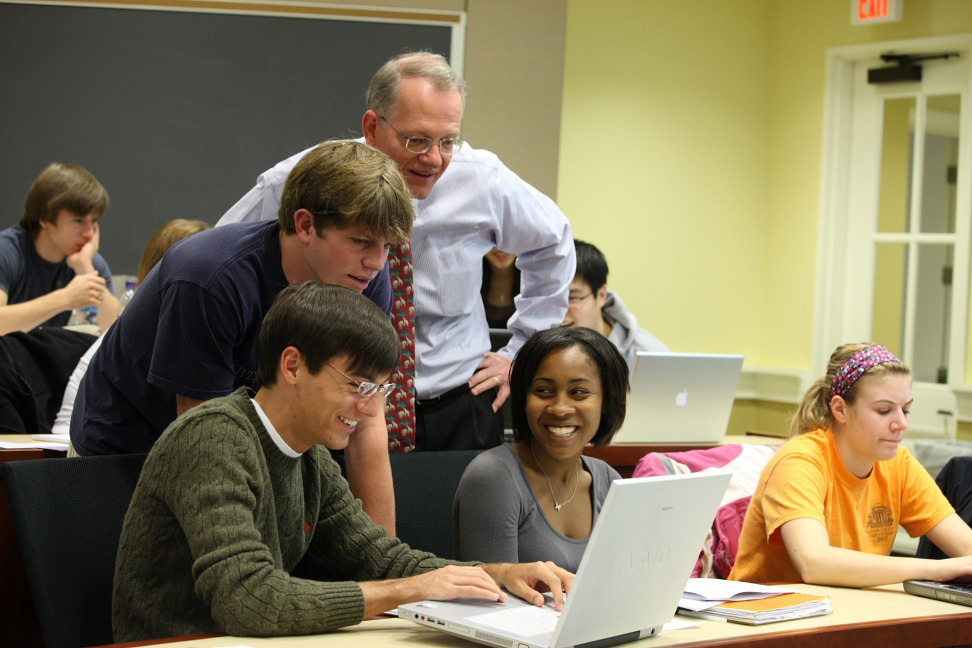 Professor standing behind students as they work on a laptop