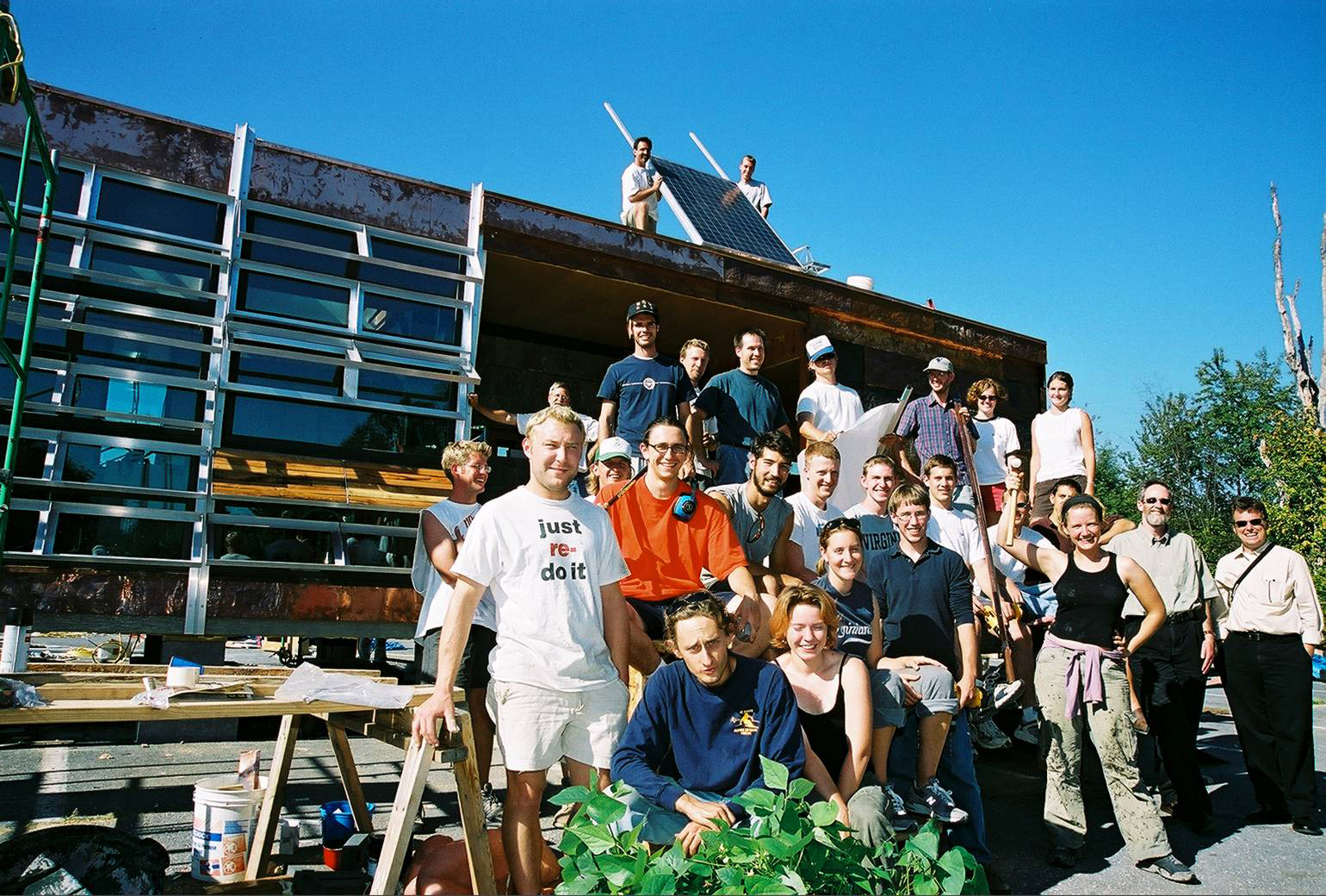 Group photo of students standing at a building while solar panels are being installed