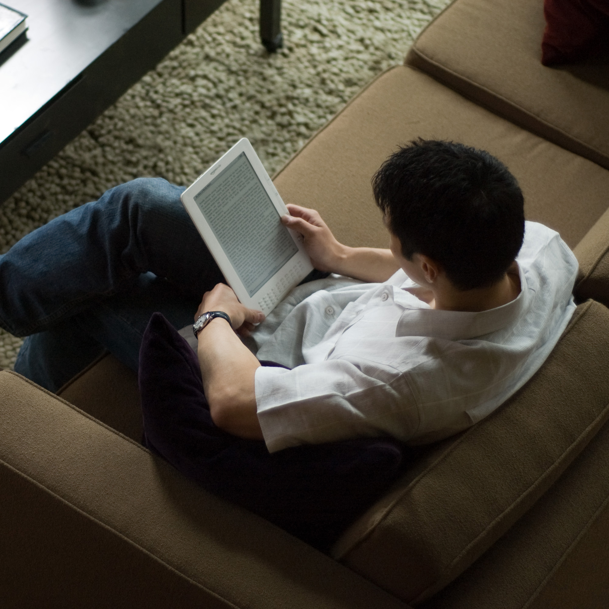 Man sitting on a couch reading a kindle device