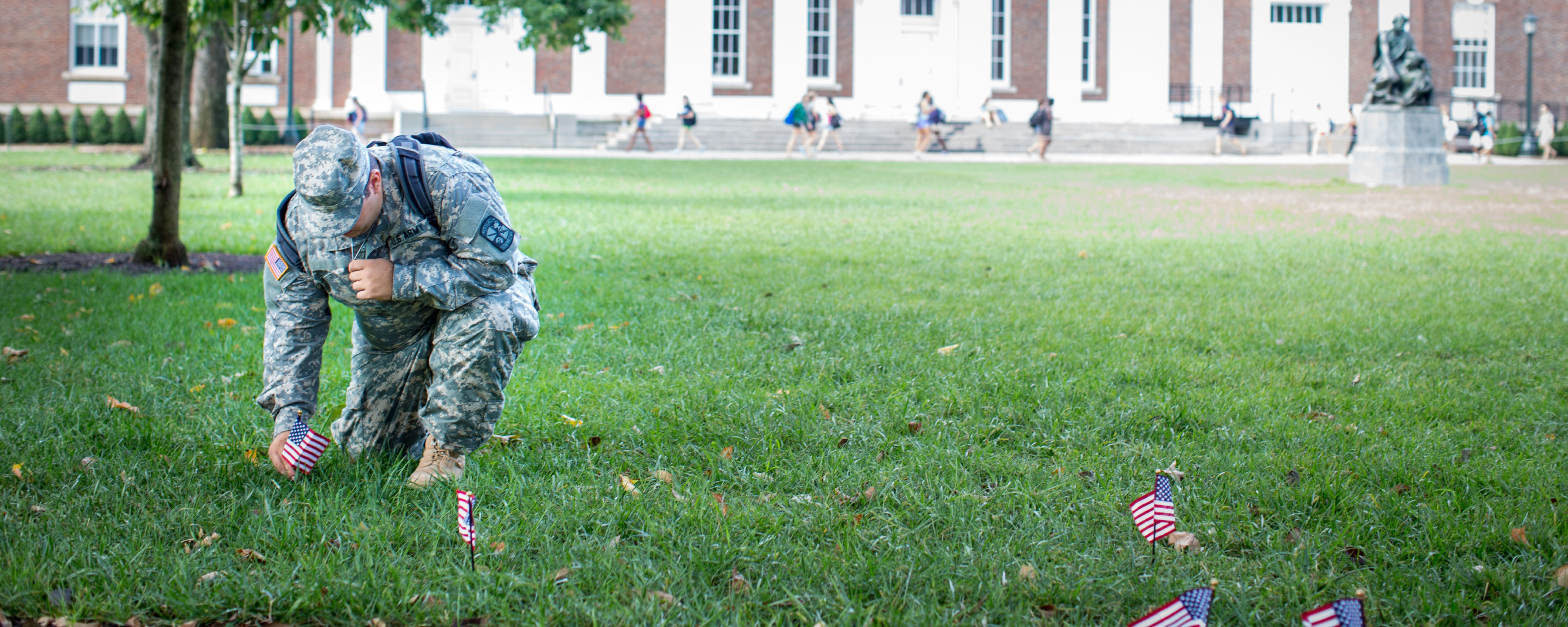 ROTC cadet kneeling on the lawn filled with American Flags