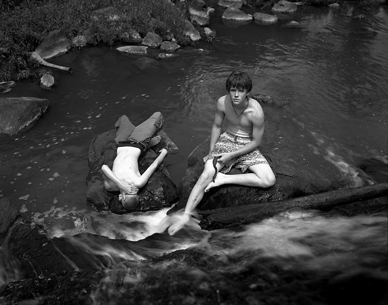 Two boys sitting on rocks in the middle of a stream