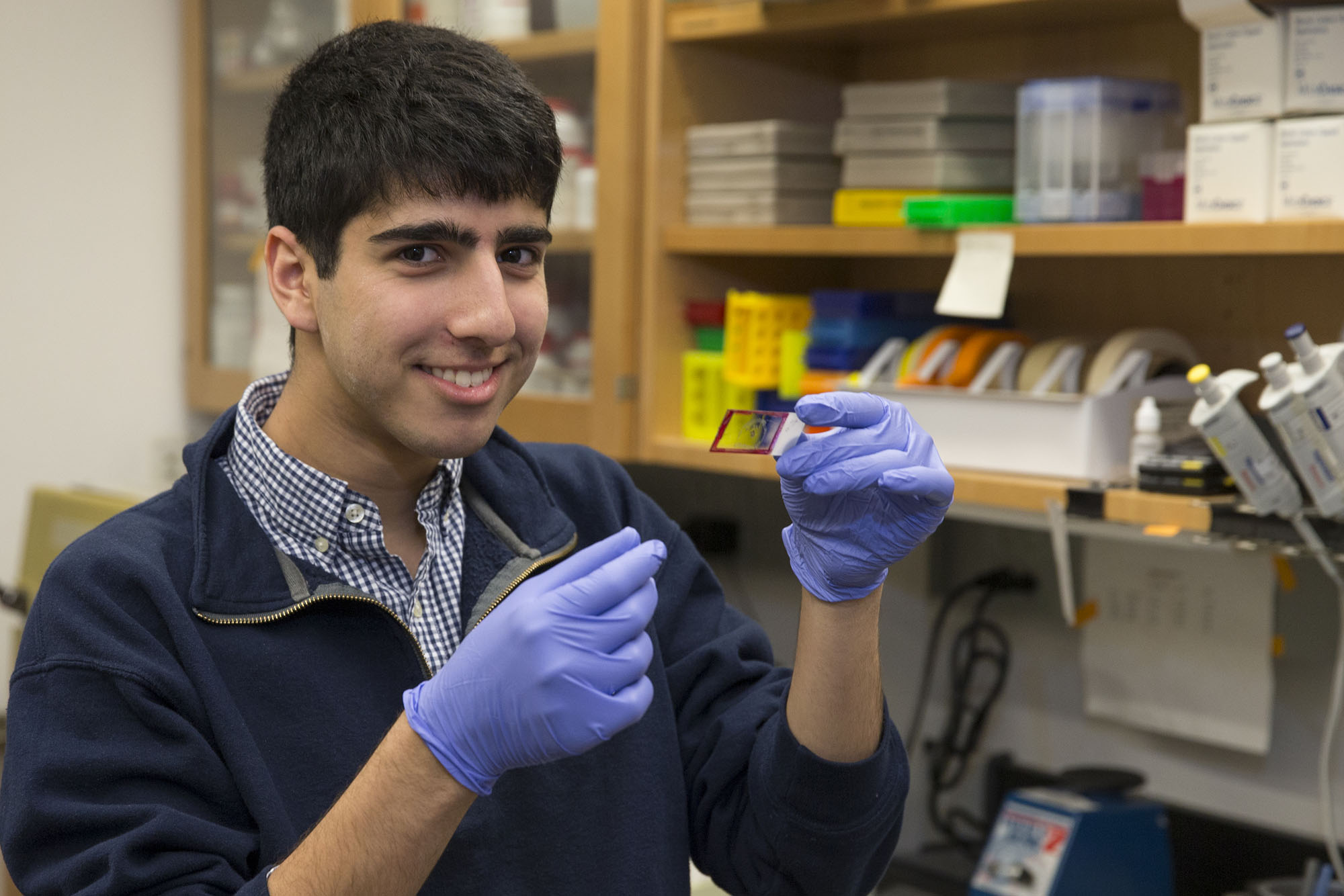 Daniel Naveed Tavakol holding a microscope slide smiling at the camera