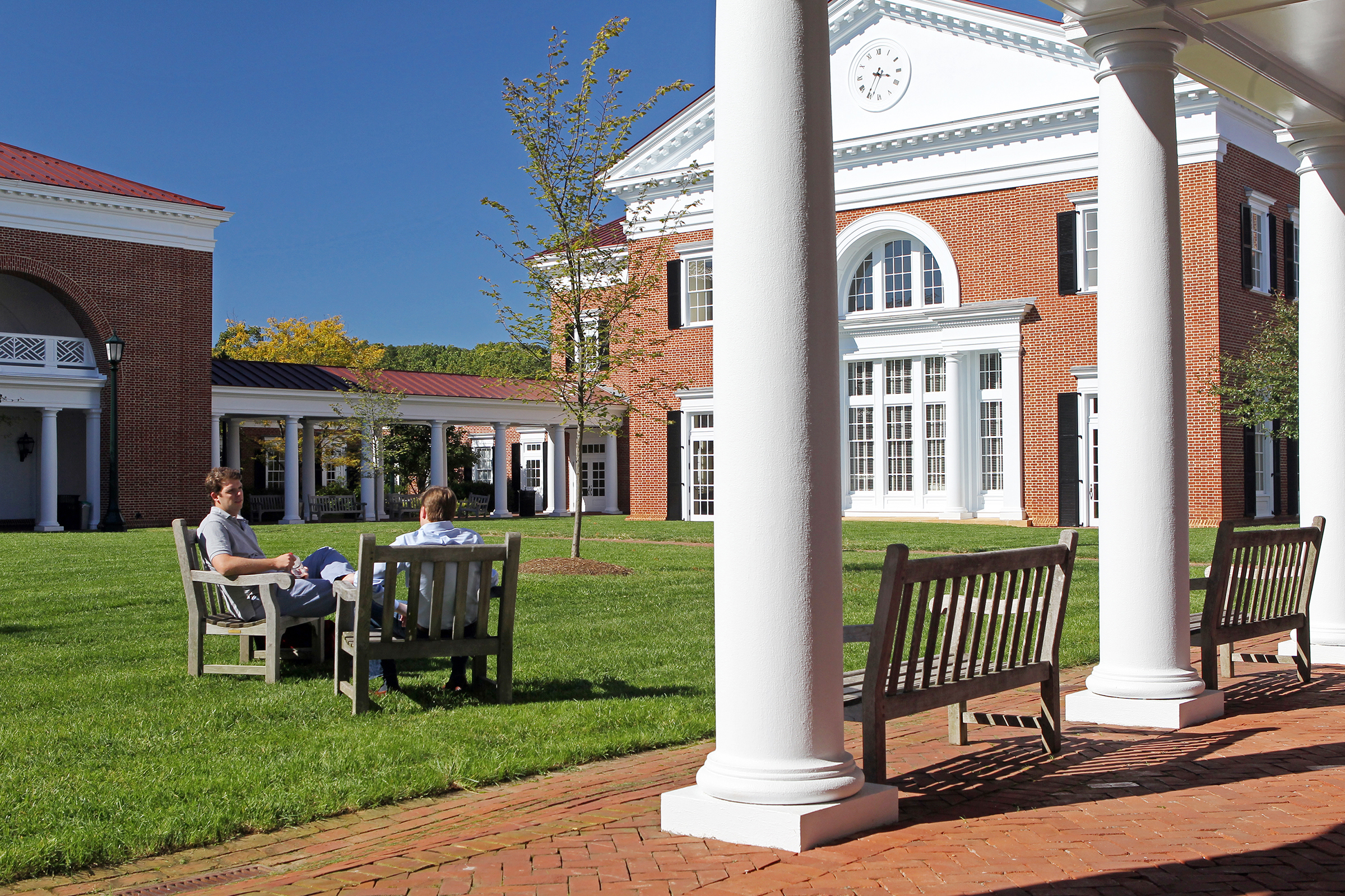 Two people sitting at benches on the Lawn in front of Darden talking