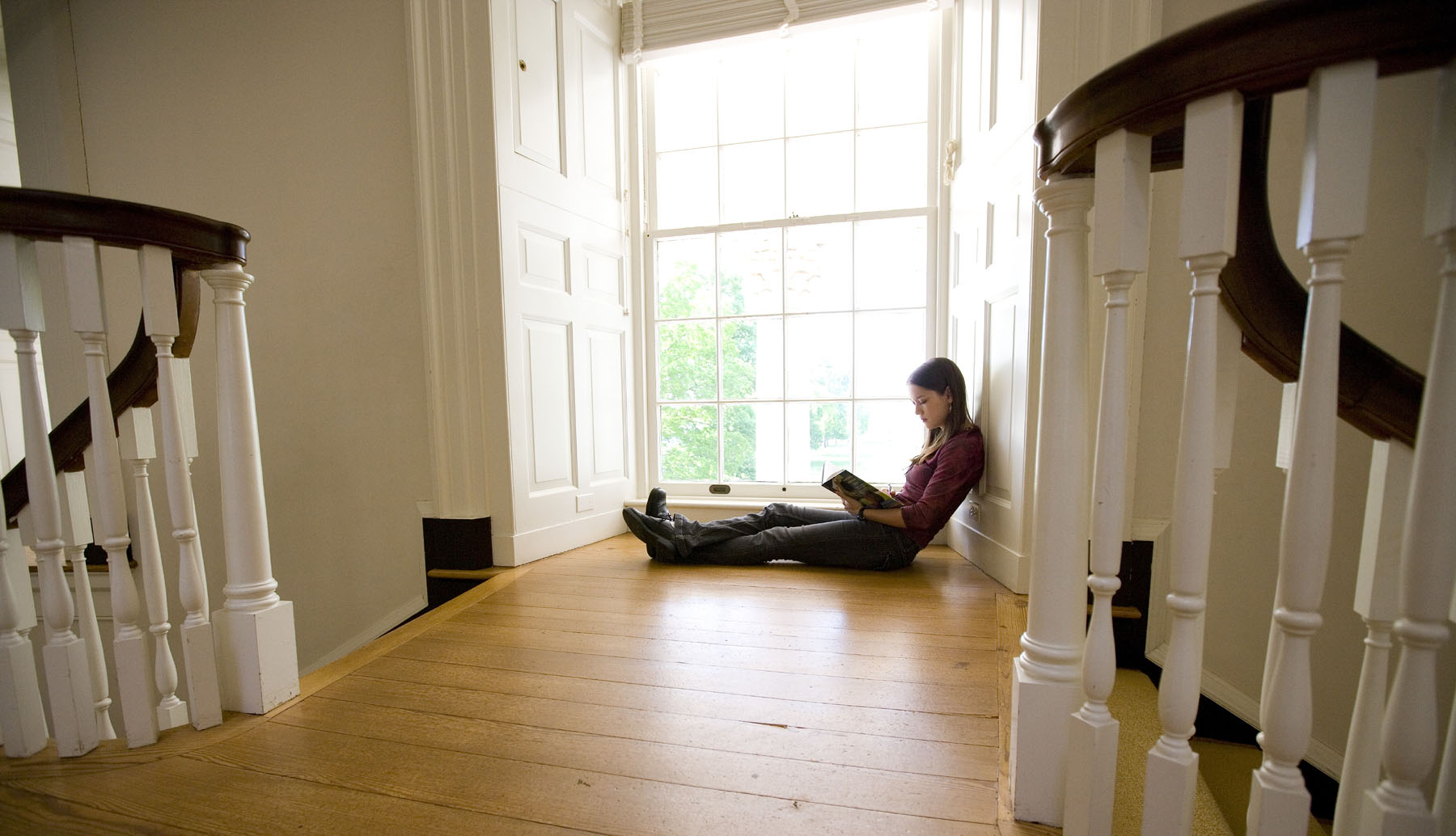 Student sits on the floor at a window reading