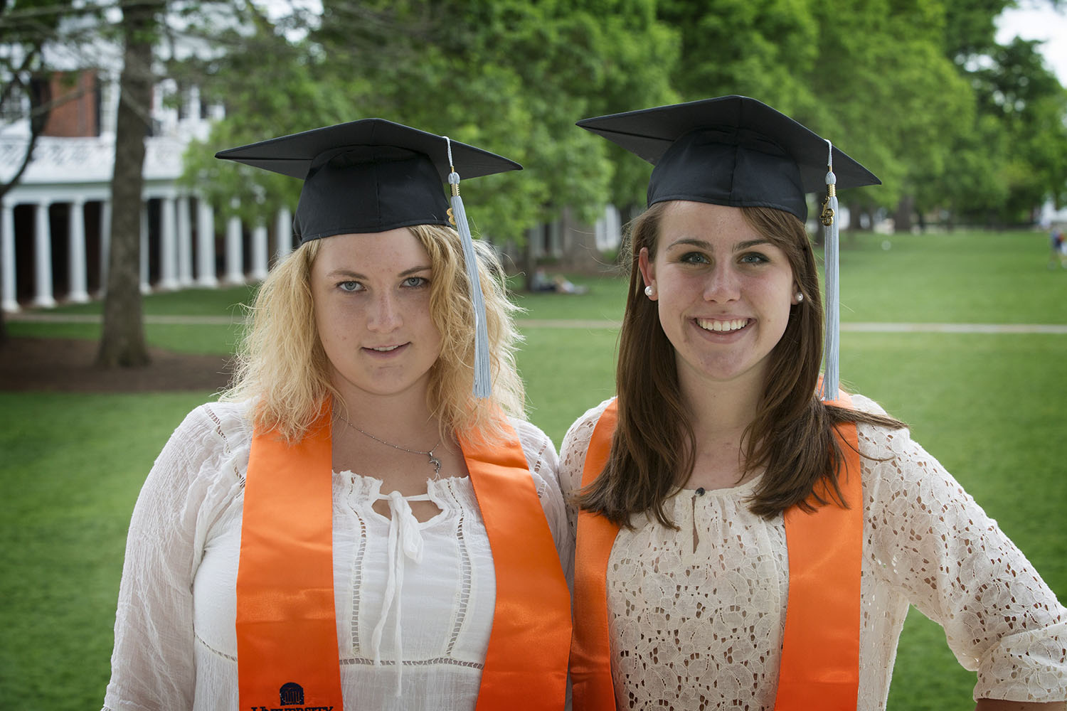 Kasey Blevins, left, and Emily Riedel, right, wears black graduation caps smiling at the camera