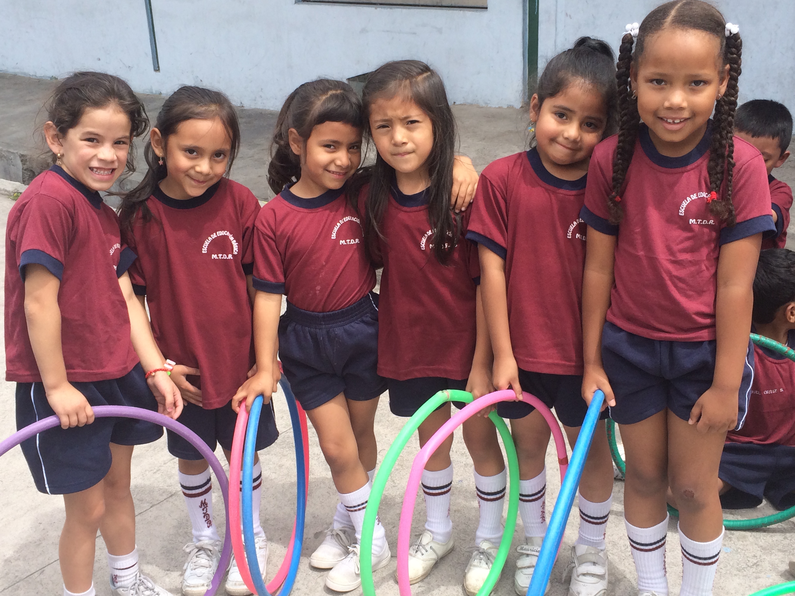 Little girls holding hula hoops stand together smiling at the camera