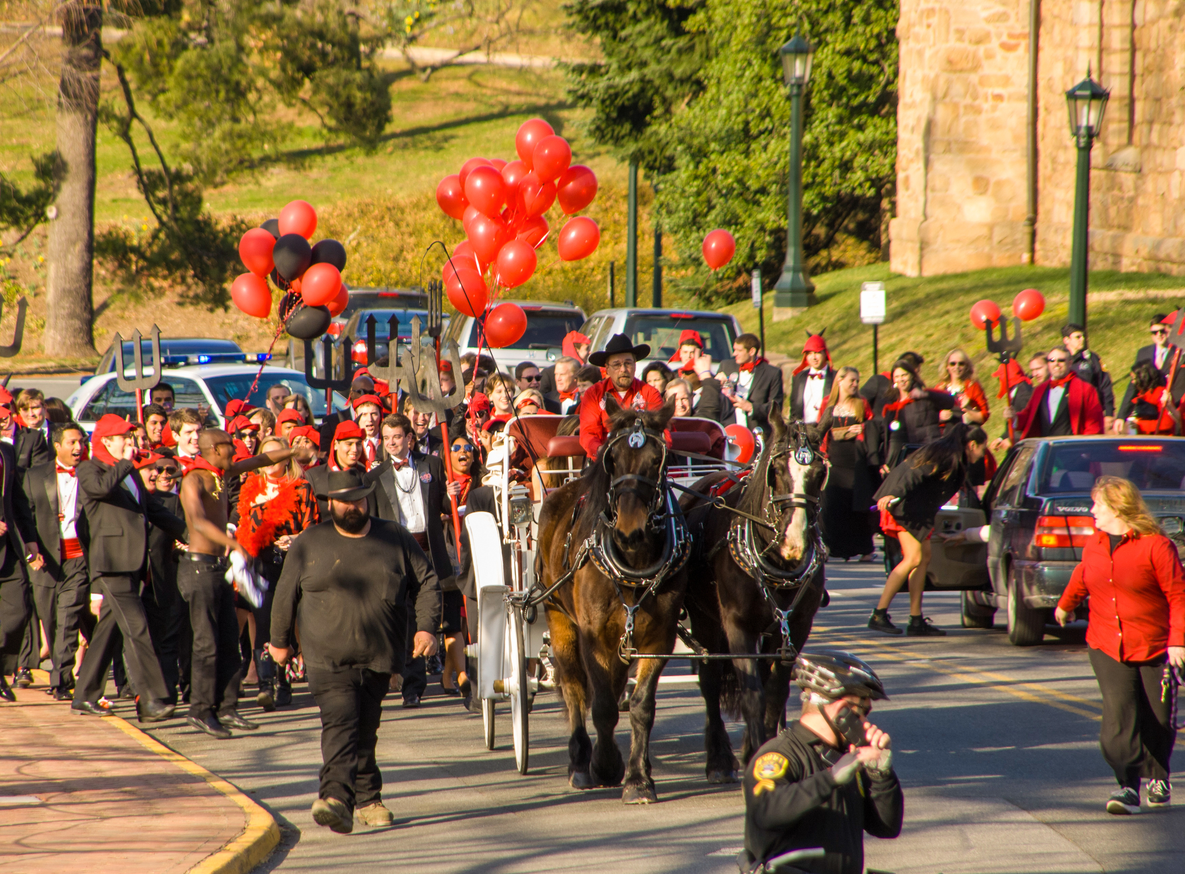 Crowd walking the street at UVA Wise wearing black and red behind a horse drawn carriage