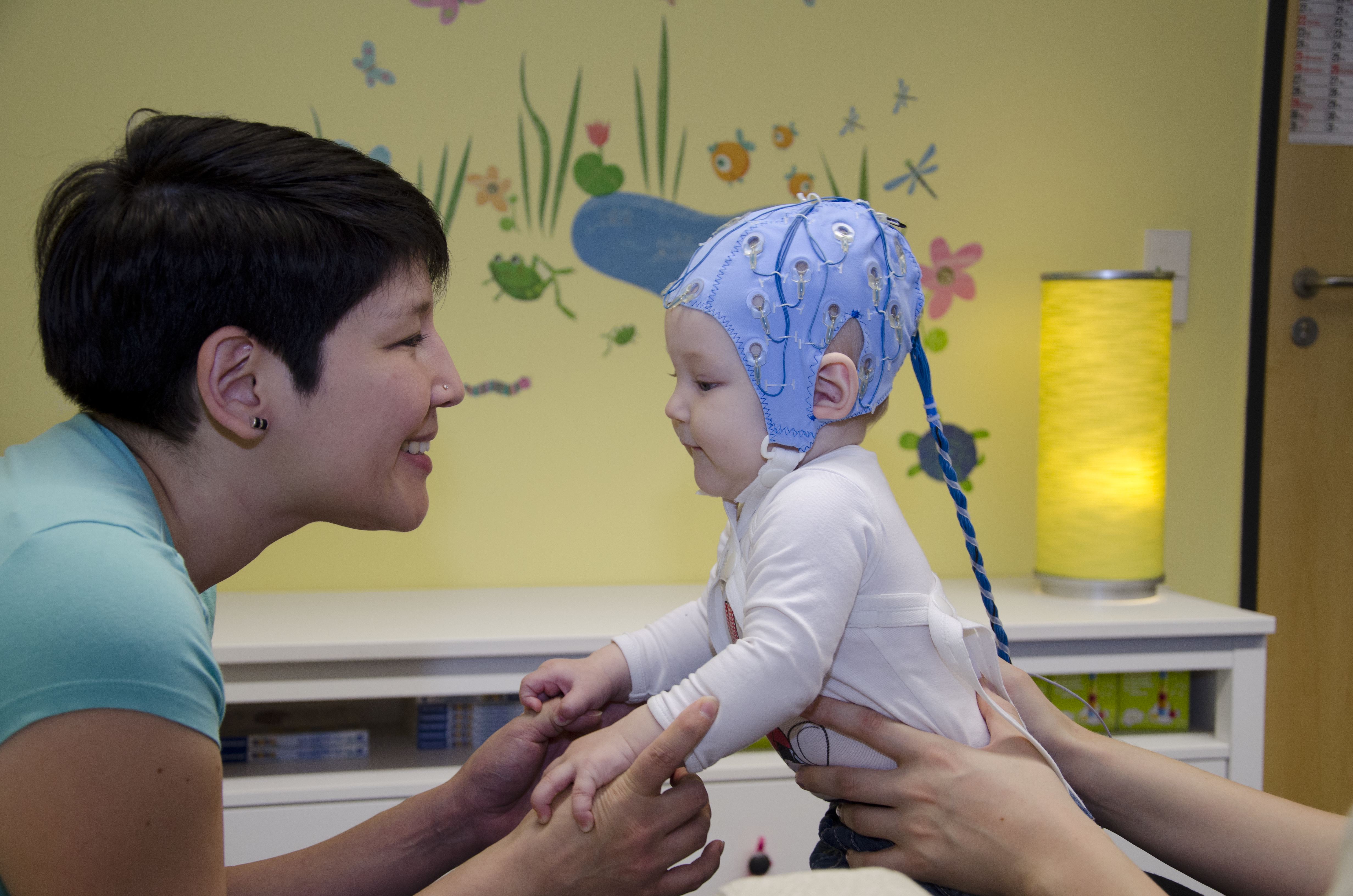 Small child wearing an EEG cap holds a womans hand