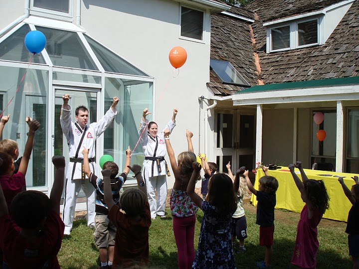 Two adults dressed in Martial Arts attire teaching small children some basic moves at a party