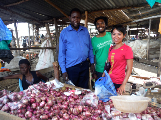 Nanetta stands in a market with two men