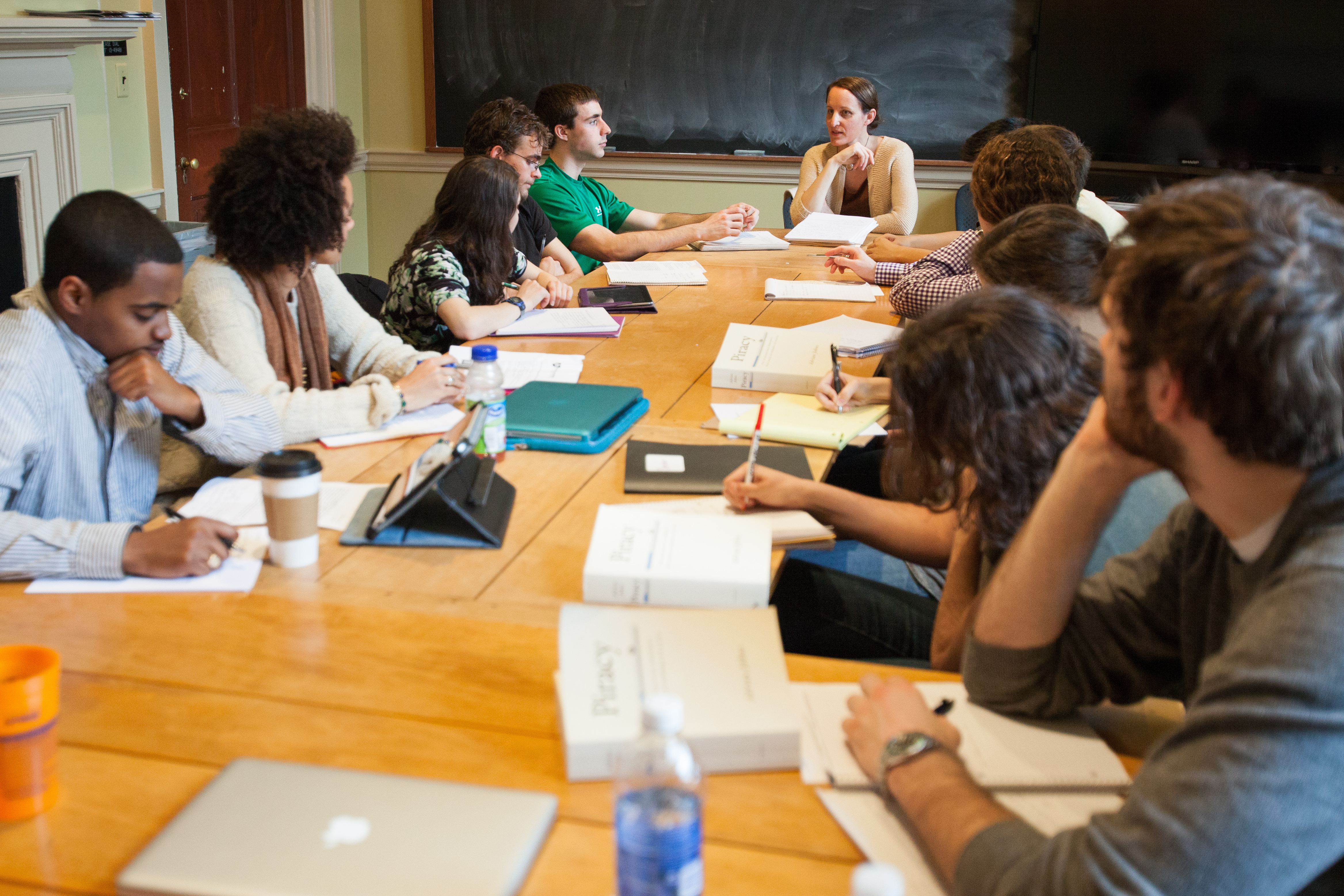 Group of people sit at a table taking notes while listening to another student talk