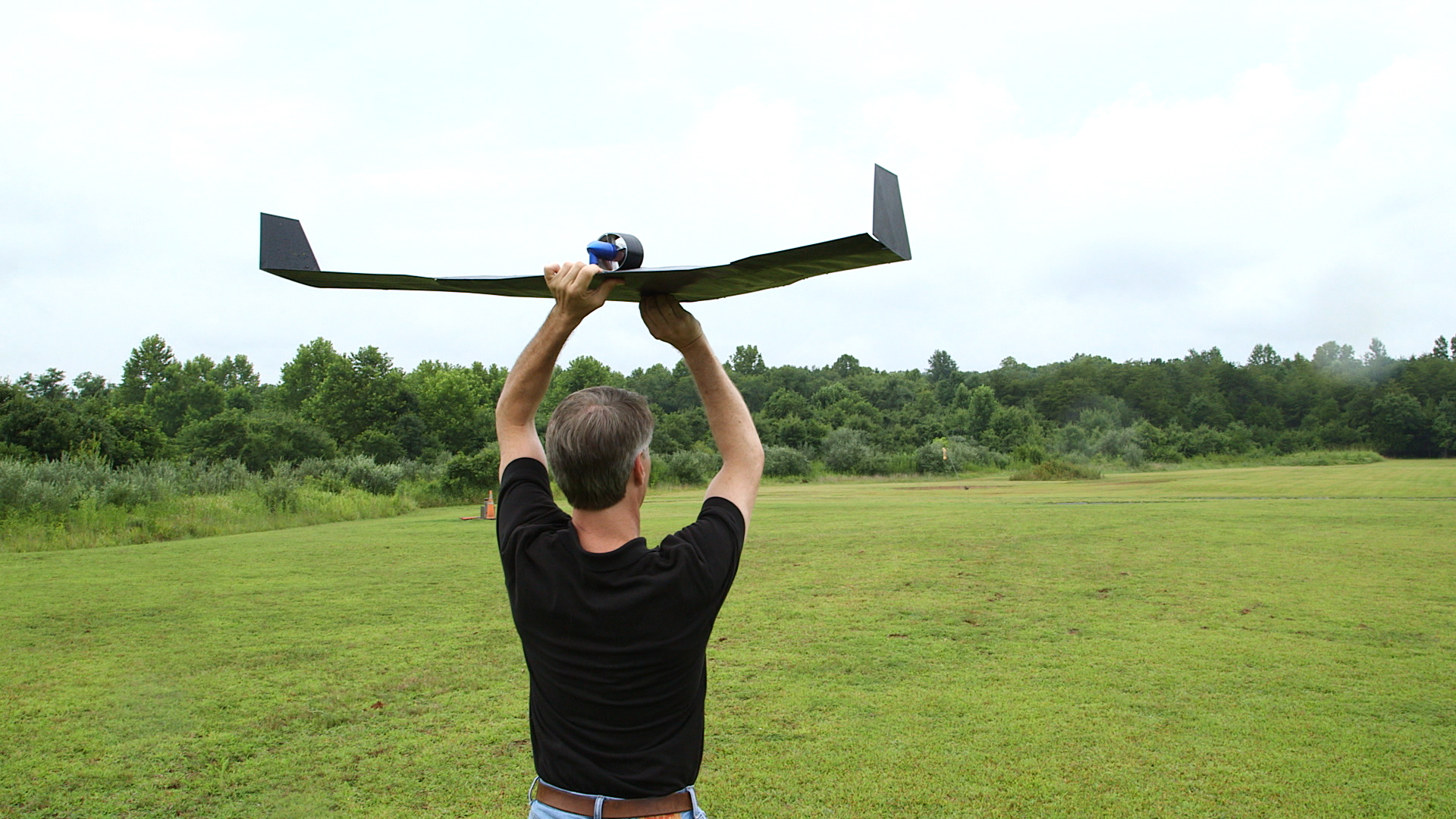 Man holds a small airplane above his head while standing in a field