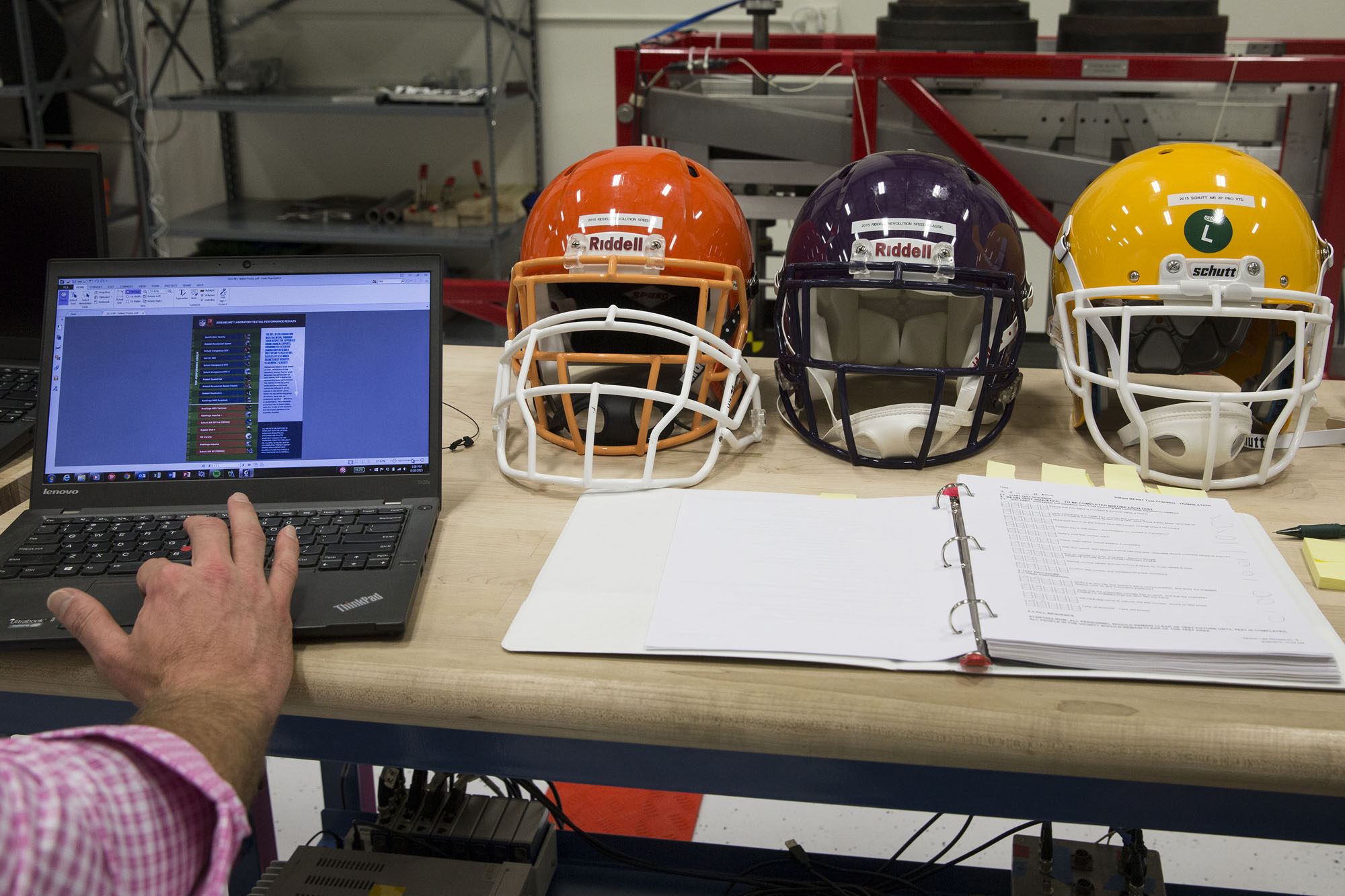 Football helmets are sitting on a table with a notebook and a person working on a laptop