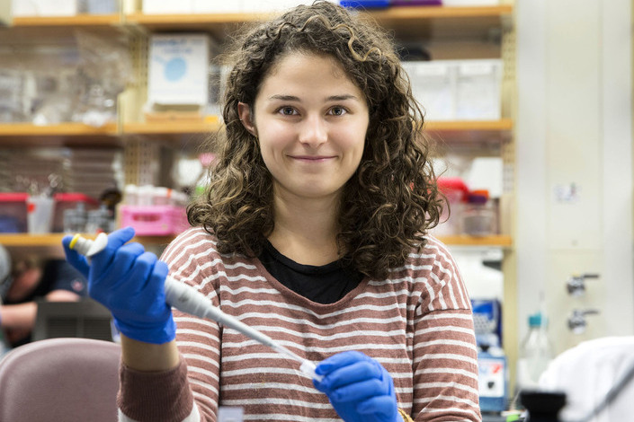 Alex Berr uses a pipet to place liquid into a test tube smiles at the camera