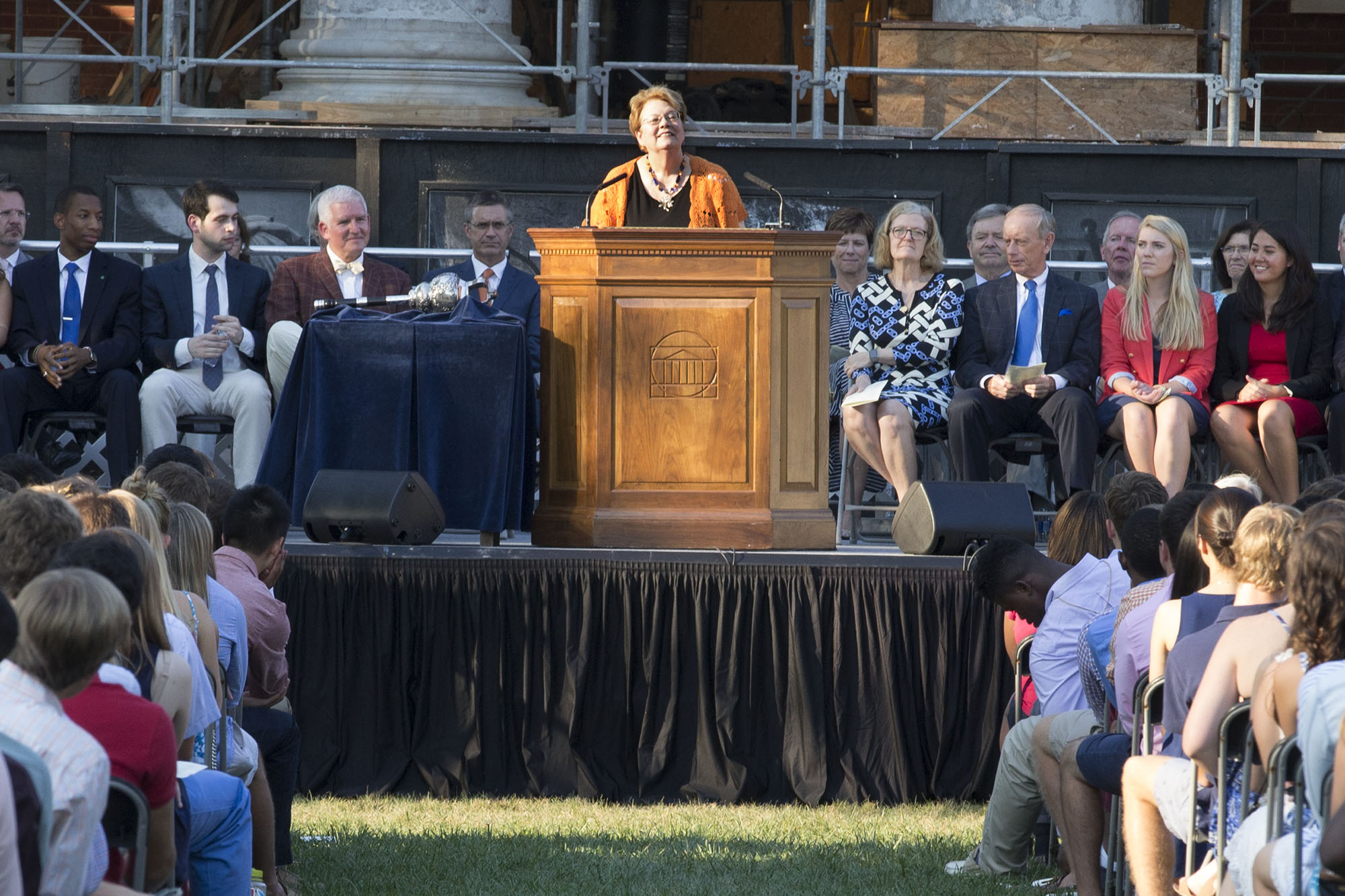 President Teresa Sullivan speaking from a podium to a group of students sitting in chairs on the lawn