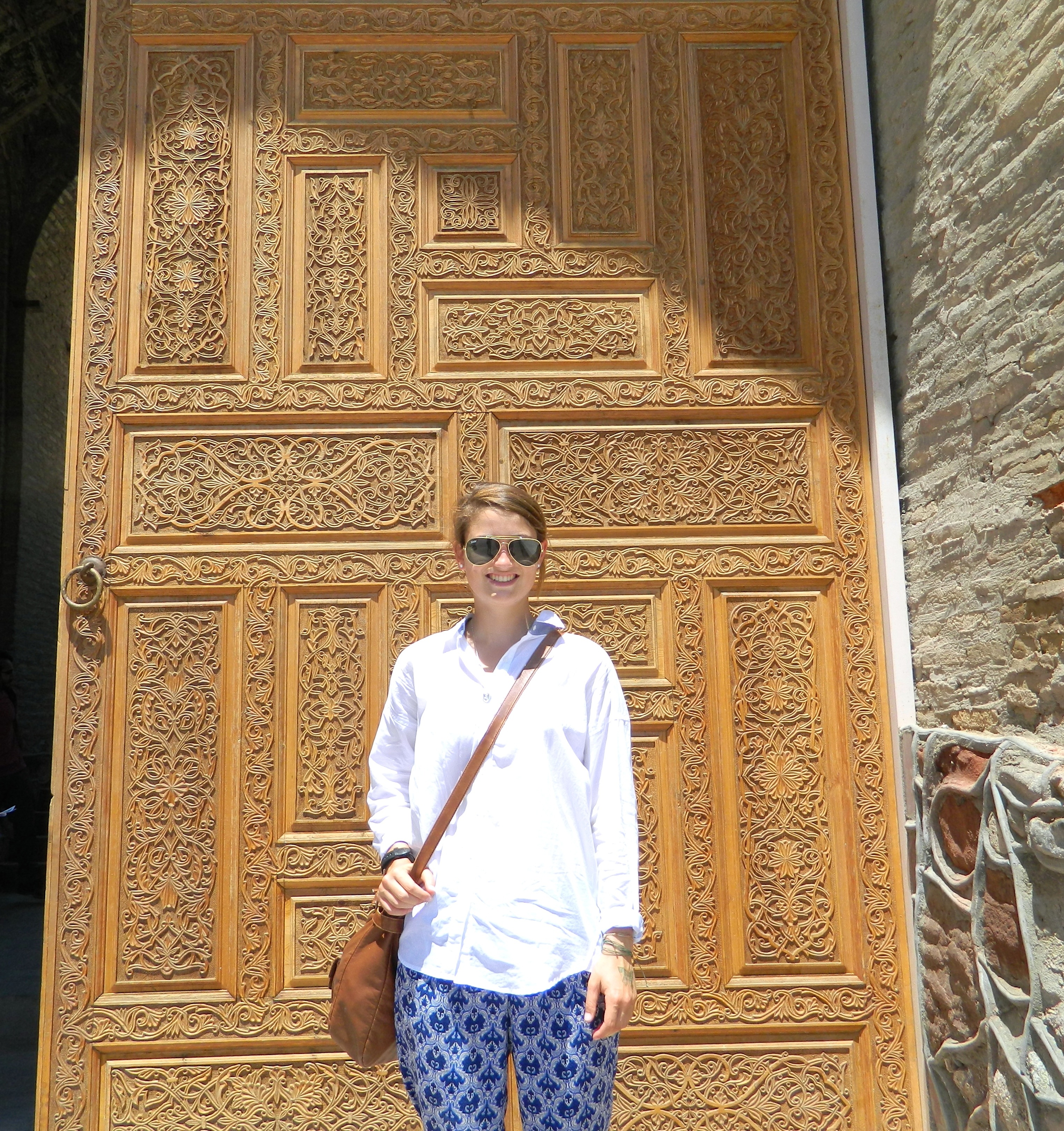 Ellen Hubbard stands in front of a huge wooden door with a very intricate design on it