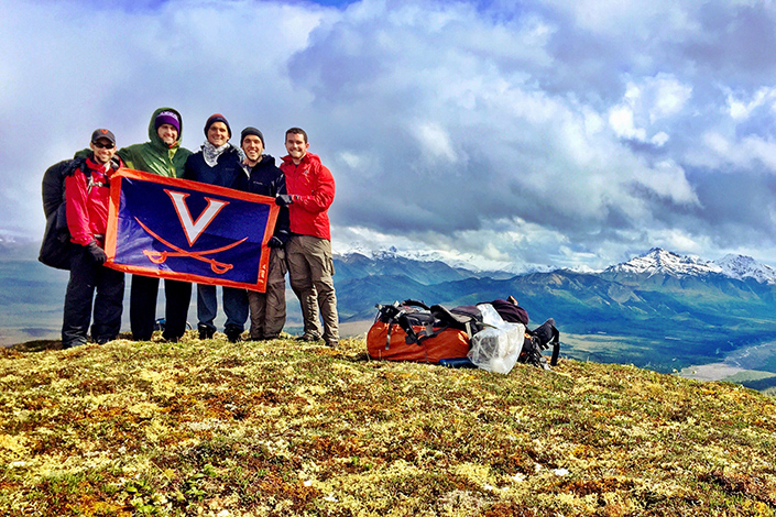 Nate Brown and four other graduates hold up a UVA v saber flag on an Alaska mountain