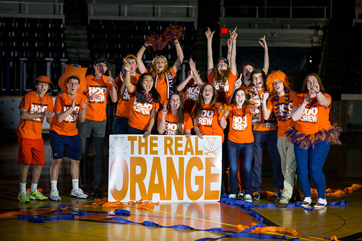 Group photo of the Hoo Crew cheering on a basketball court with a sign in front of them that says the Real Orange