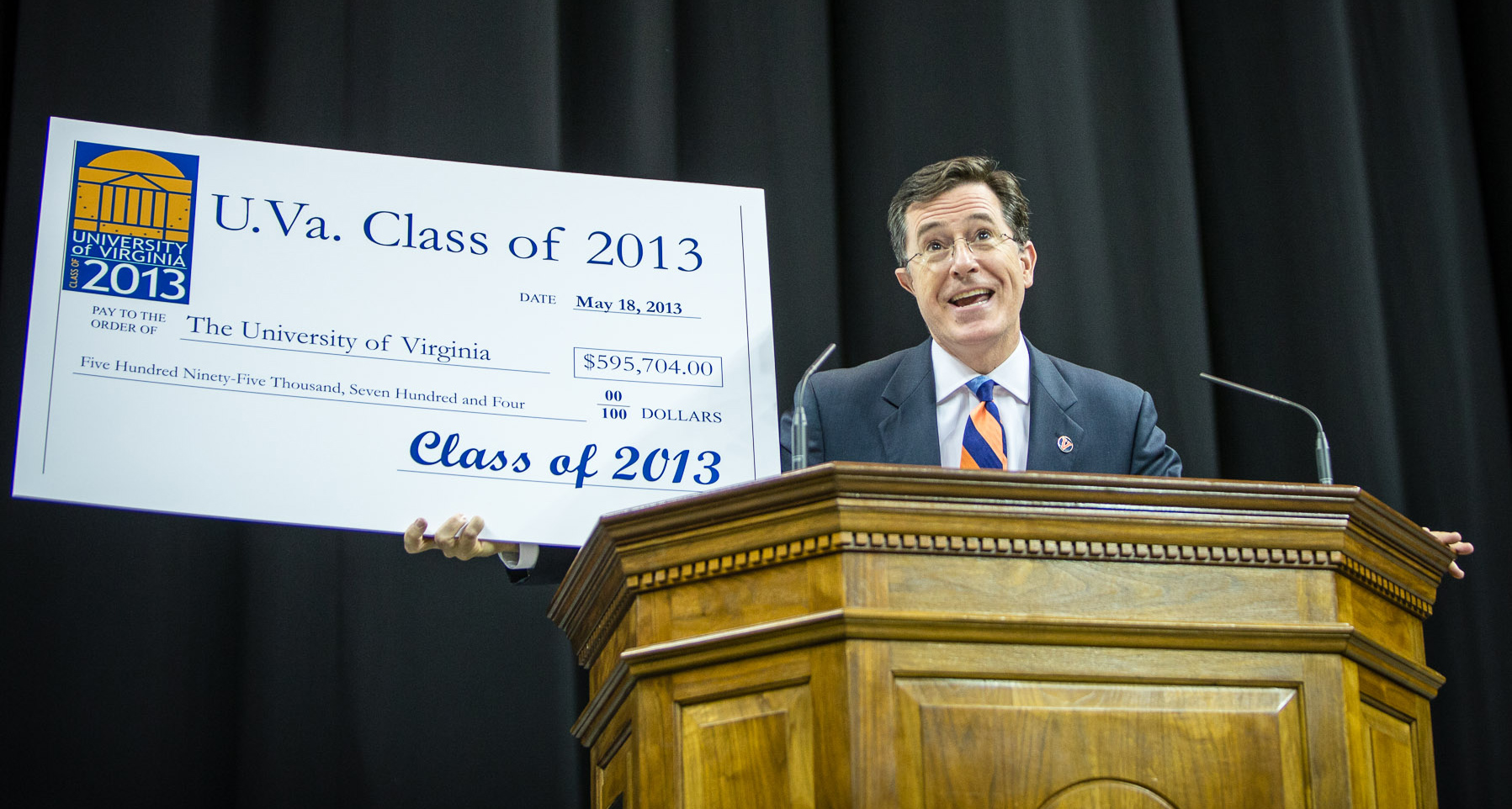 Stephen Colbert holds up a check from a podium while giving a speech