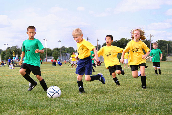 Little children running on a field kicking a soccer ball