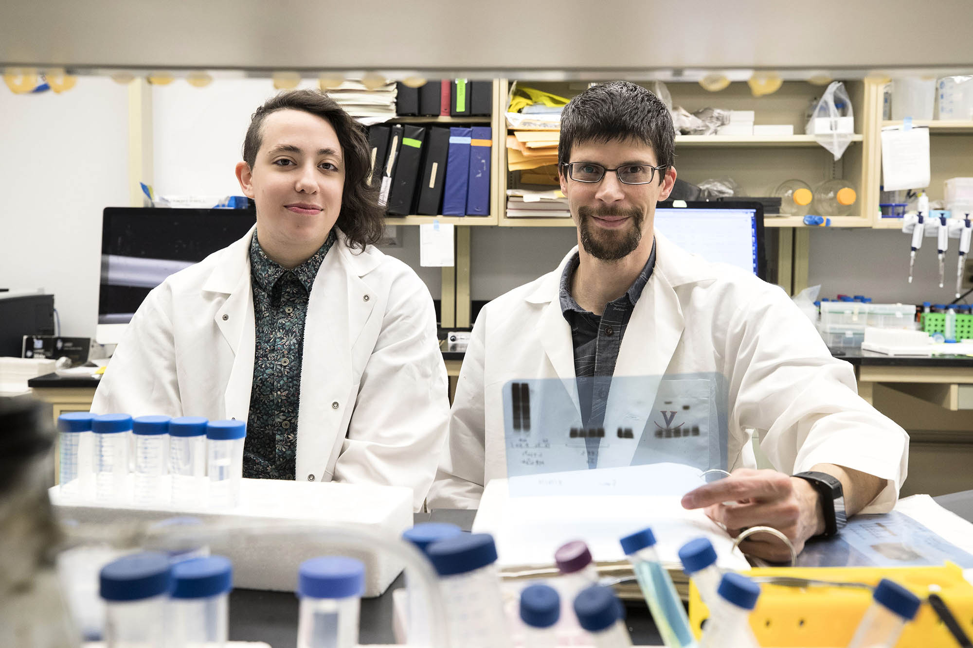 Dorian Rosen, left, and Alban Gaultier, right sit at a table in the lab together working on test tubes and looking through a binder