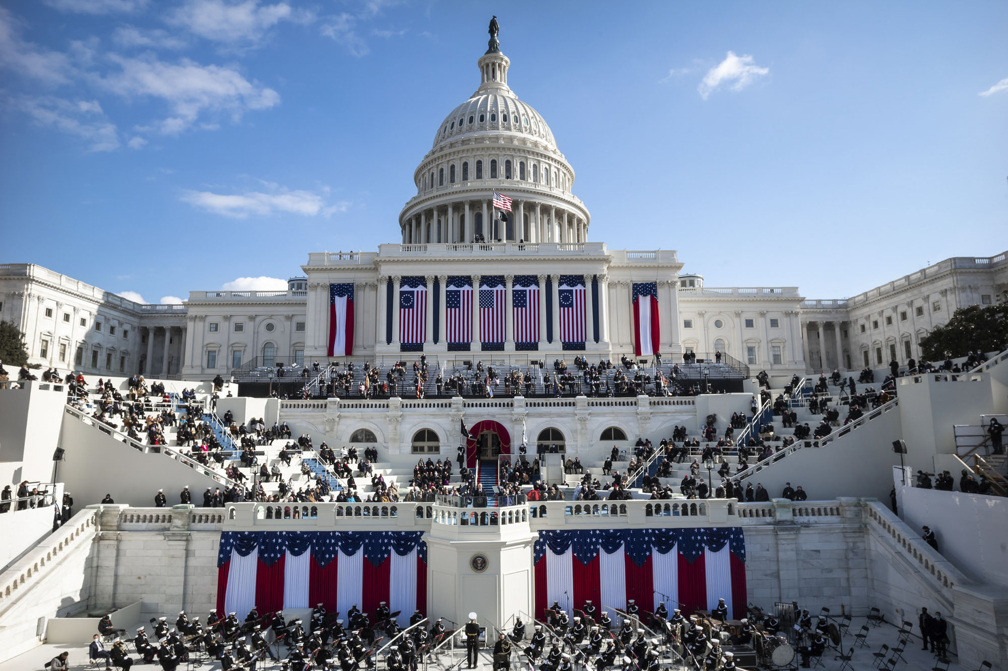 United States Capitol building building with American Flags hanging down and people social distanced for the presidential inauguration