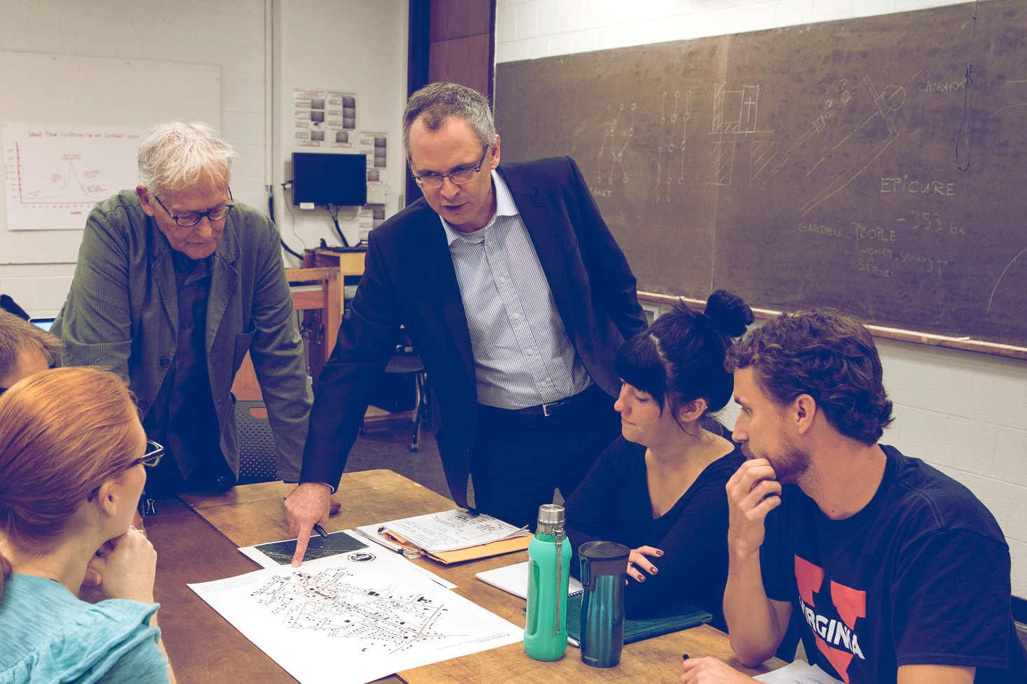 Johnston, standing at right, and Philippe Revault, left, talk with students while pointing to paper plans on the table
