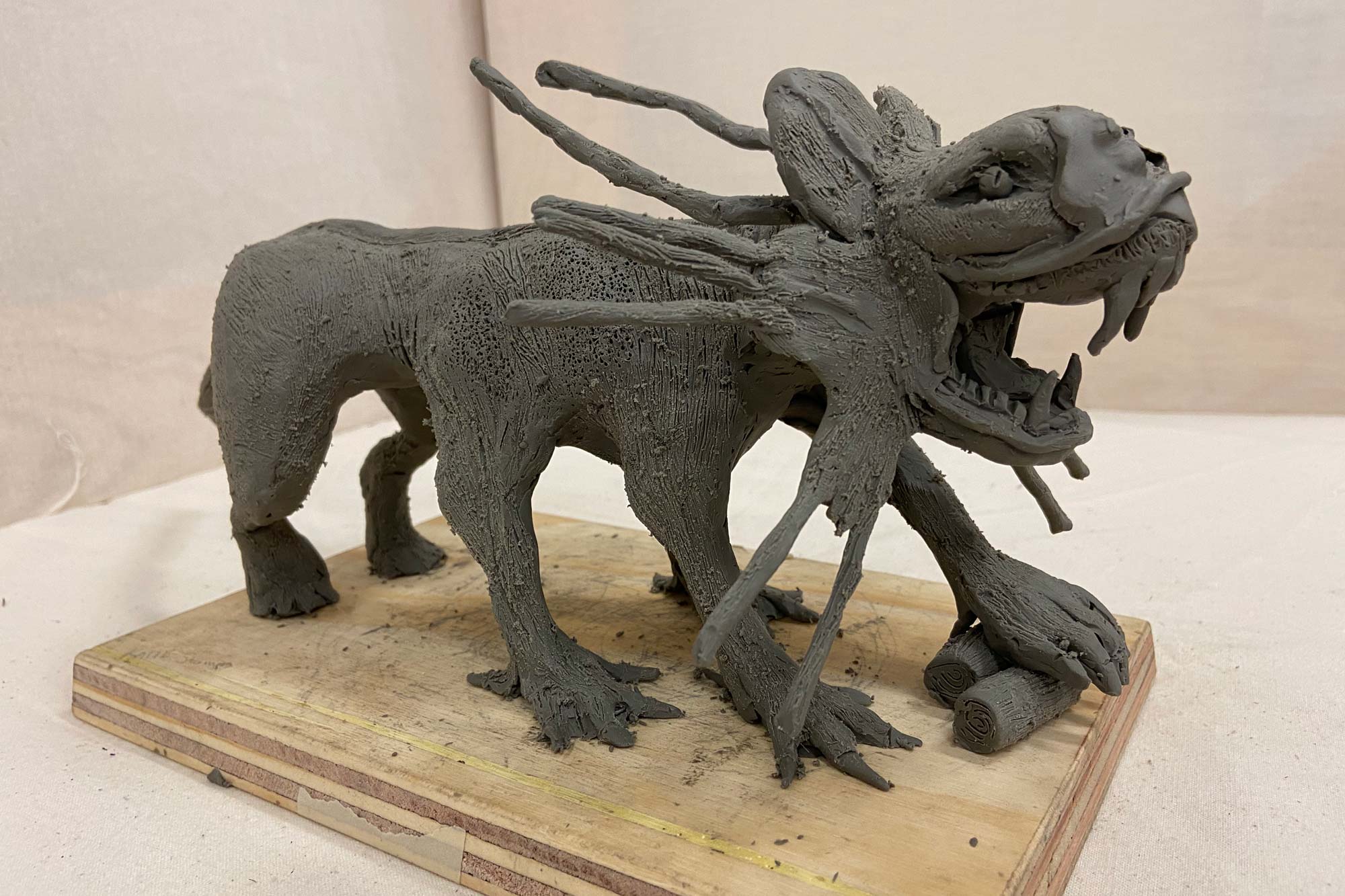 Grey Clay sculture of a 6 legged beast with sharp teeth and spikes coming out of its head