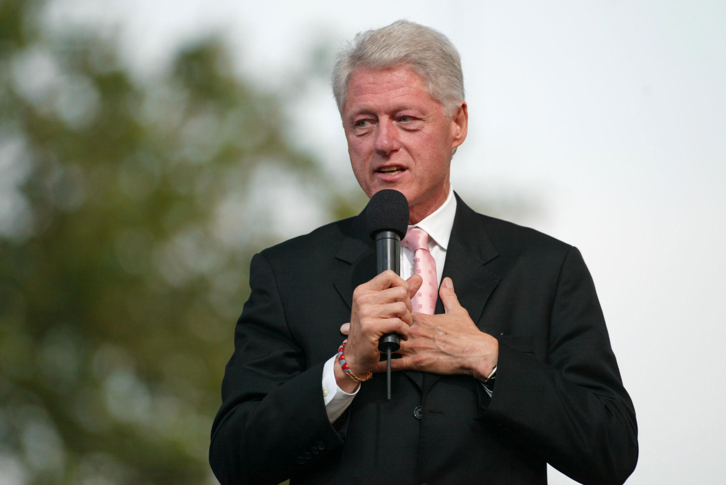 Bill Clinton standing on stage speaking into a microphone