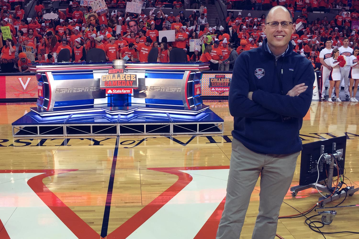 Bill Hofheimer standing on the basketball court with the College Gameday stage behind him