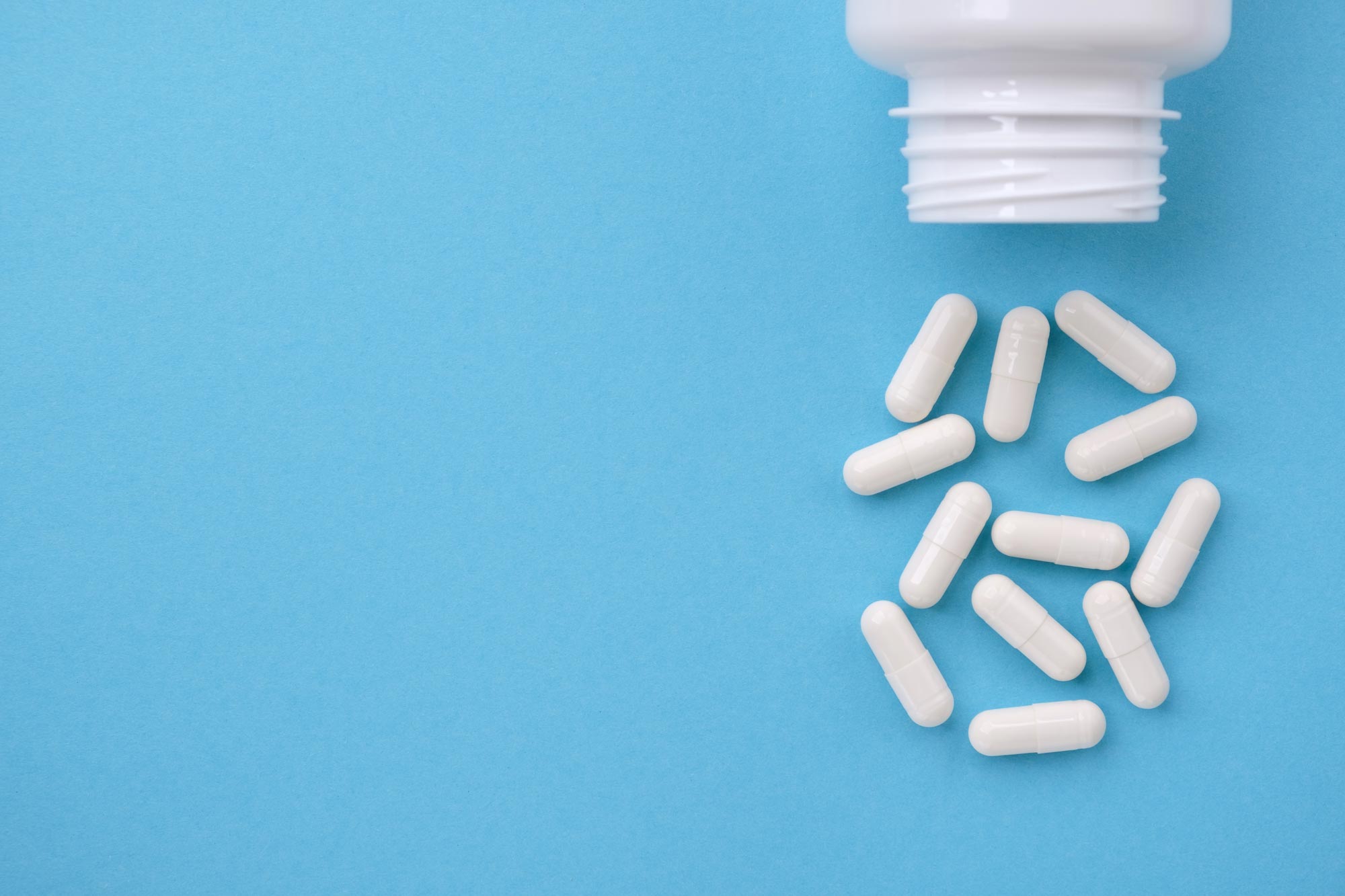 White pills dumped out of a bottle onto a light blue background