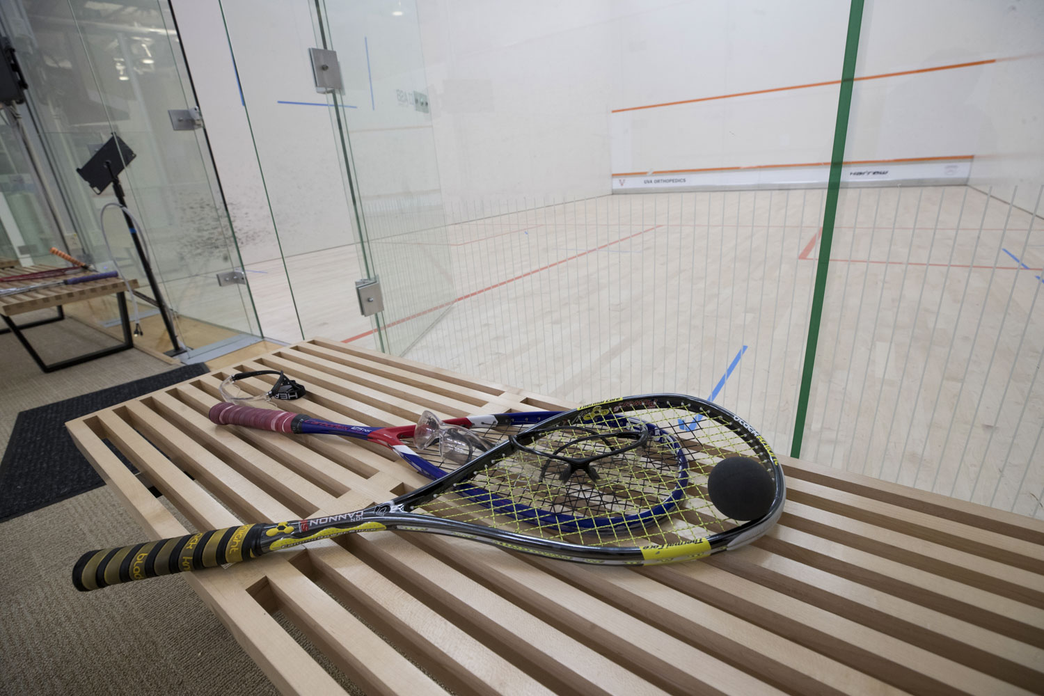 Squash racquets and a ball sitting on a bench outside of the glass enclosed squash court