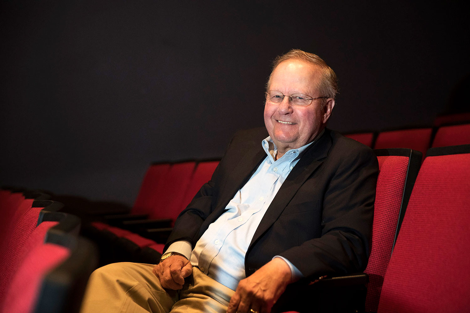 Robert Chapel sitting in a red theatre chair smiling at the camera