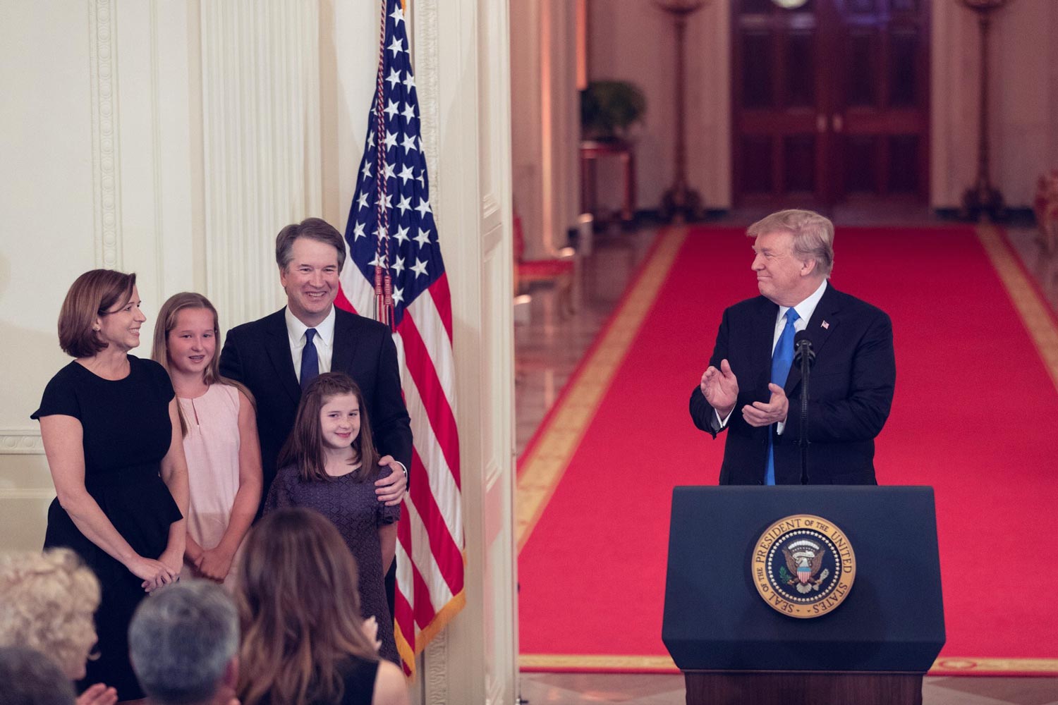 President Donal Trump clapping at a podium looking at Brett Kavanaugh and his family. 