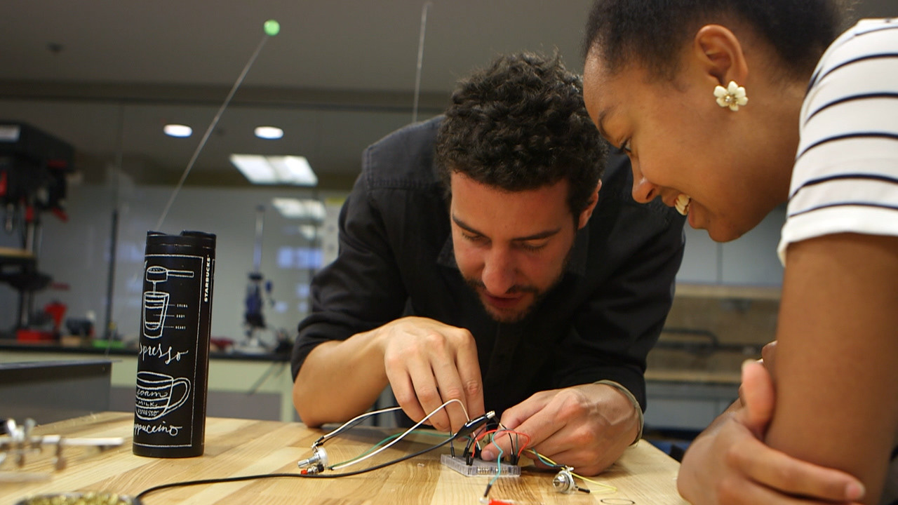Peter Bussigel working with a student on an electrical board at a table
