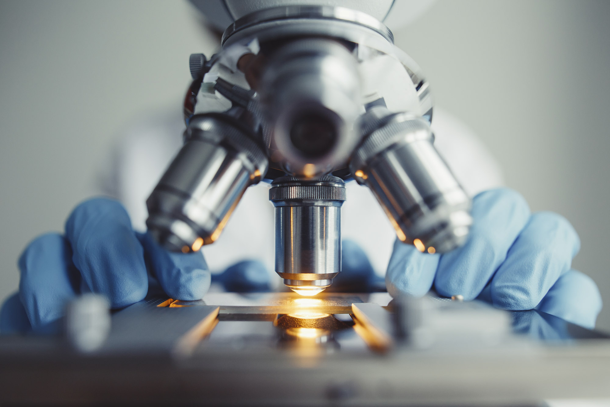 Microscope looking at a slide with gloved hands holding the slide