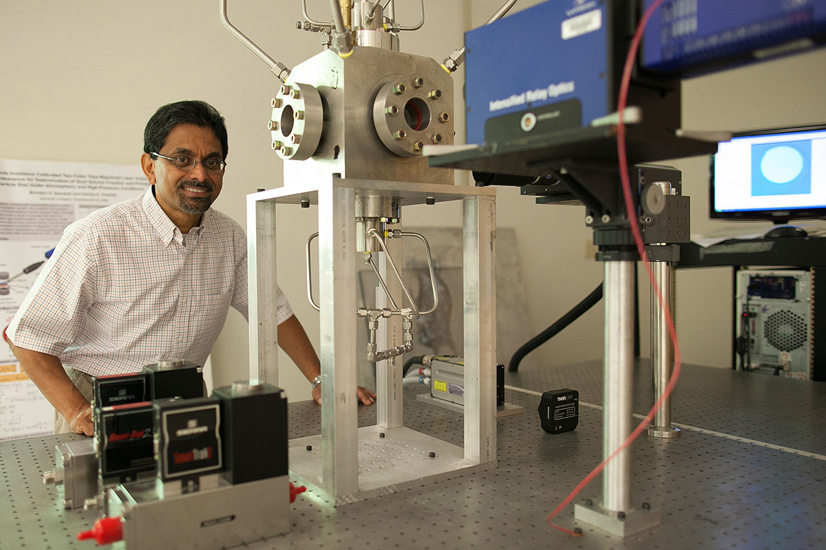 Harsha Chelliah stands in the lab next to a machine smiling at the camera