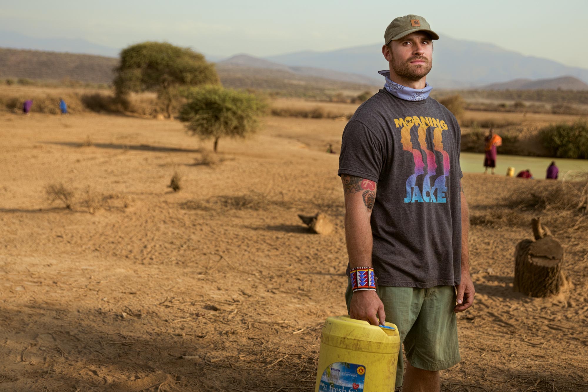 Chris Long stands in the Africa desert near a watering hole carrying a yellow bucket to fill up with water