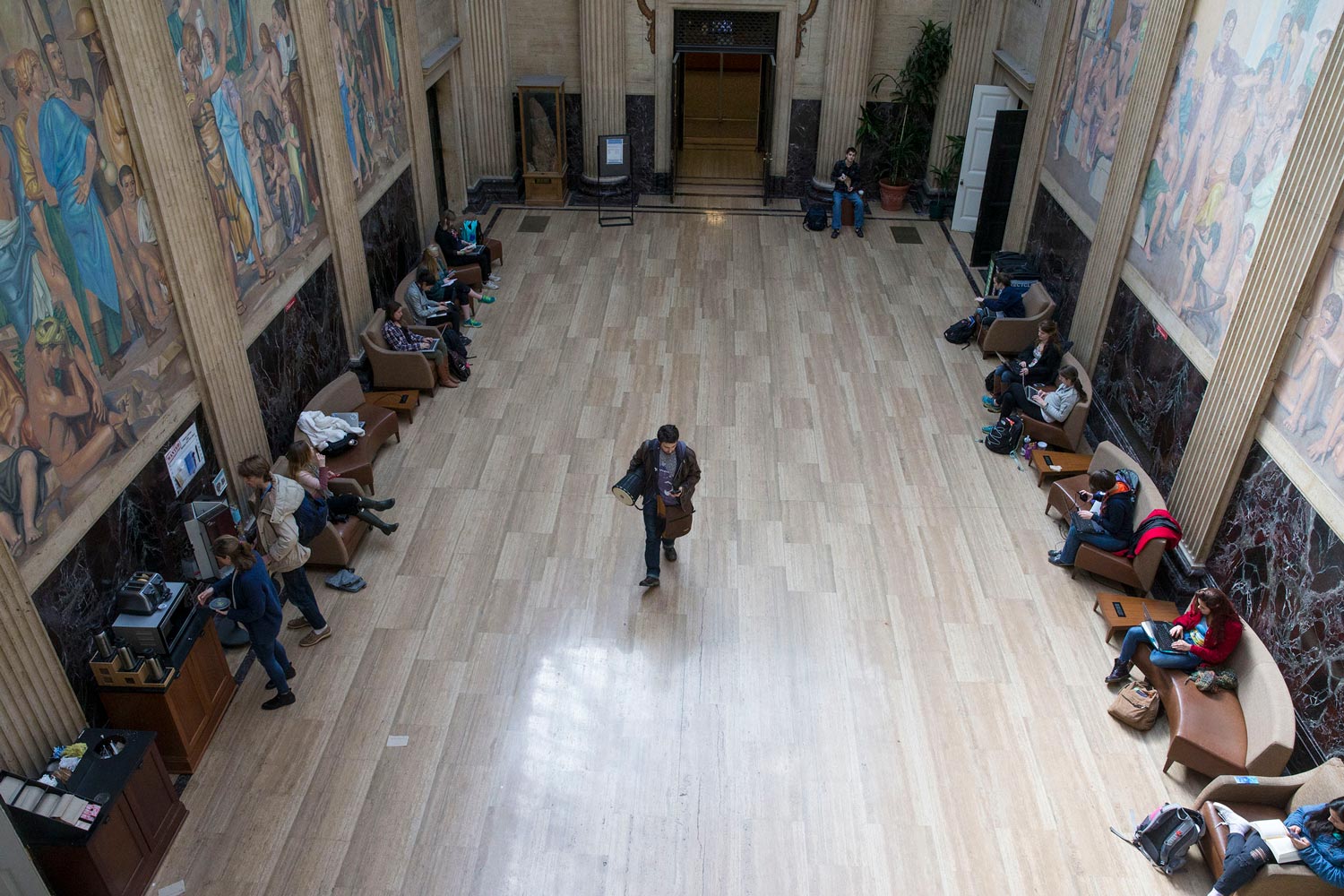 Students working in a hallway in Clark Hall lined with floor to ceiling paintings