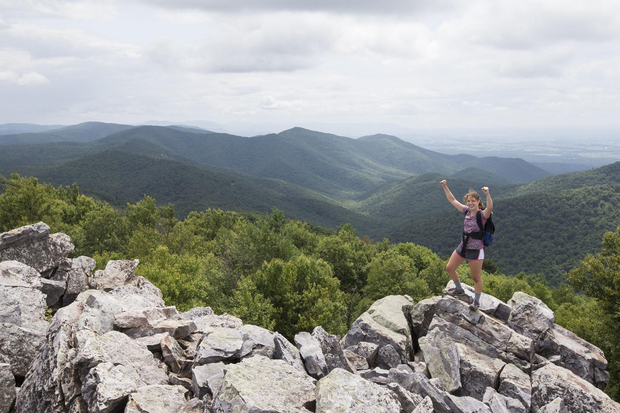 Female student with arms raised as she stands on top of boulders overlooking the Shenandoah Valley
