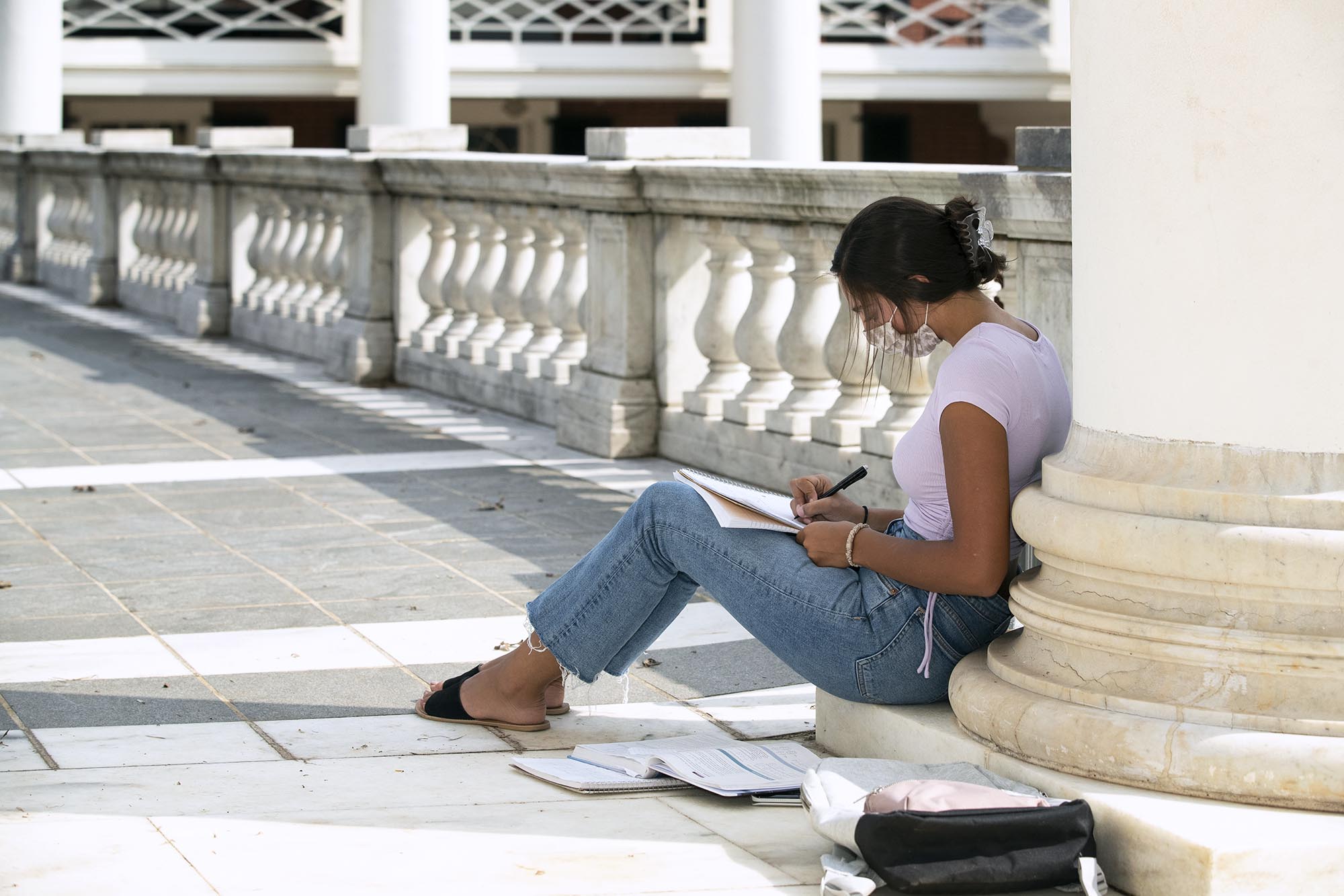 Student sitting at the base of a column at the Rotunda working  on her school work
