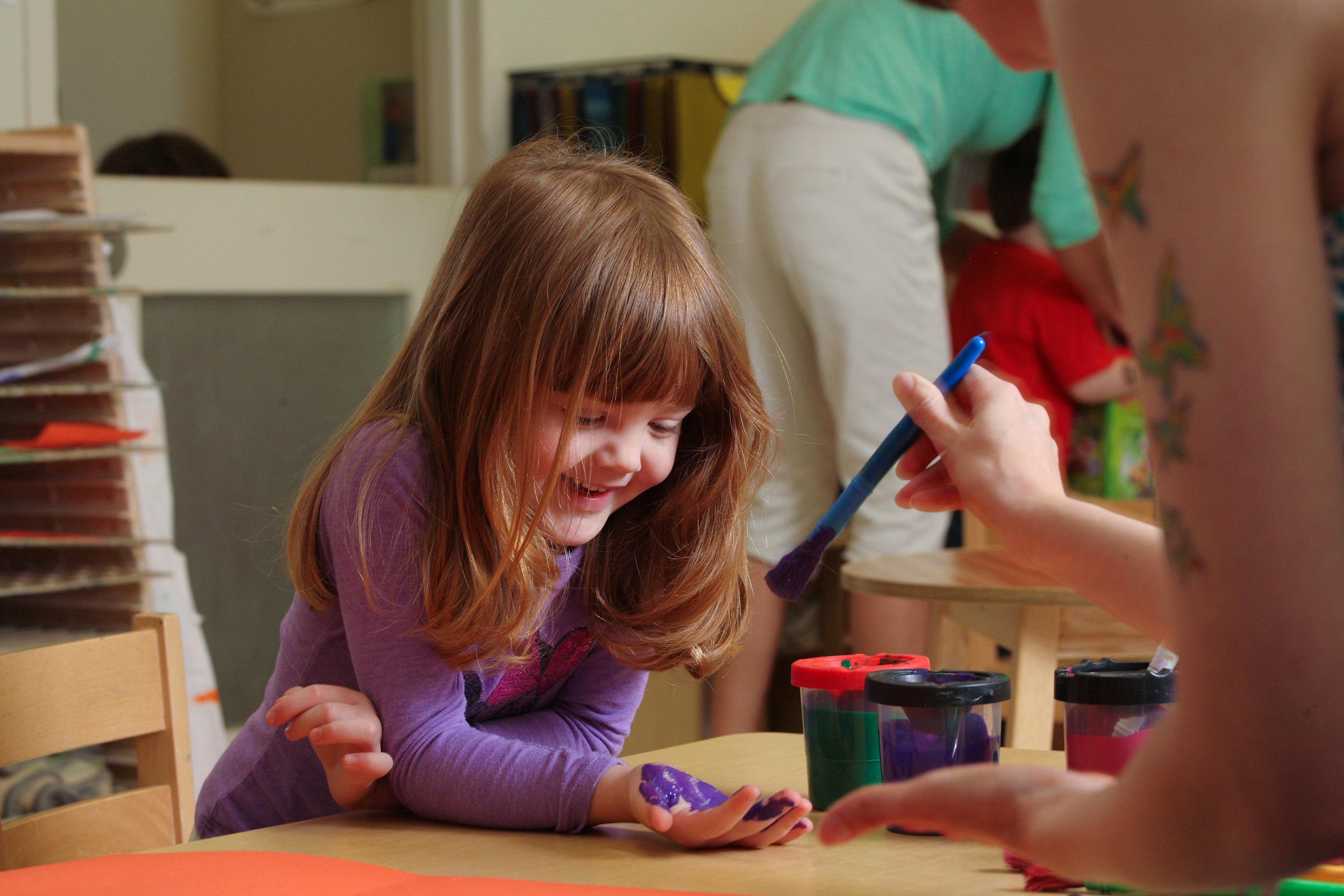 Child letting an adult paint their hand in purple