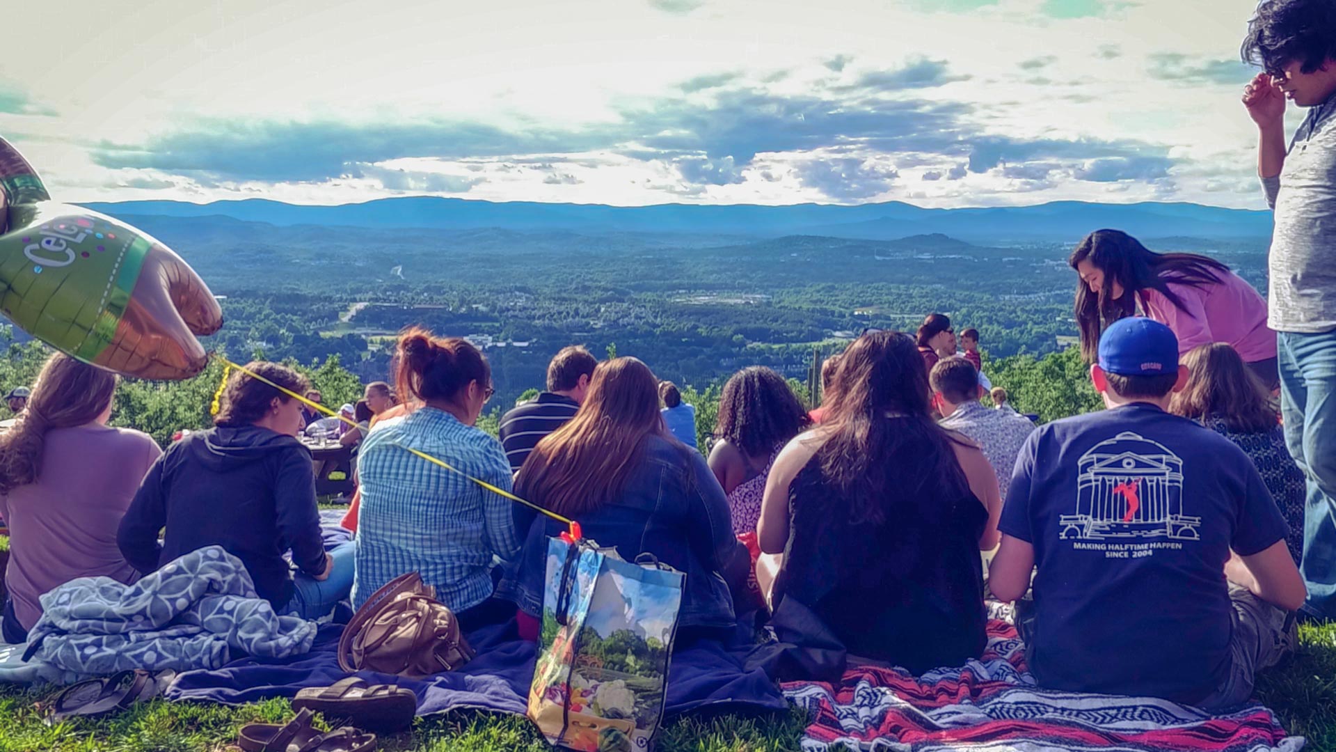 Group of students sitting on the ground on blankets on top of a mountain
